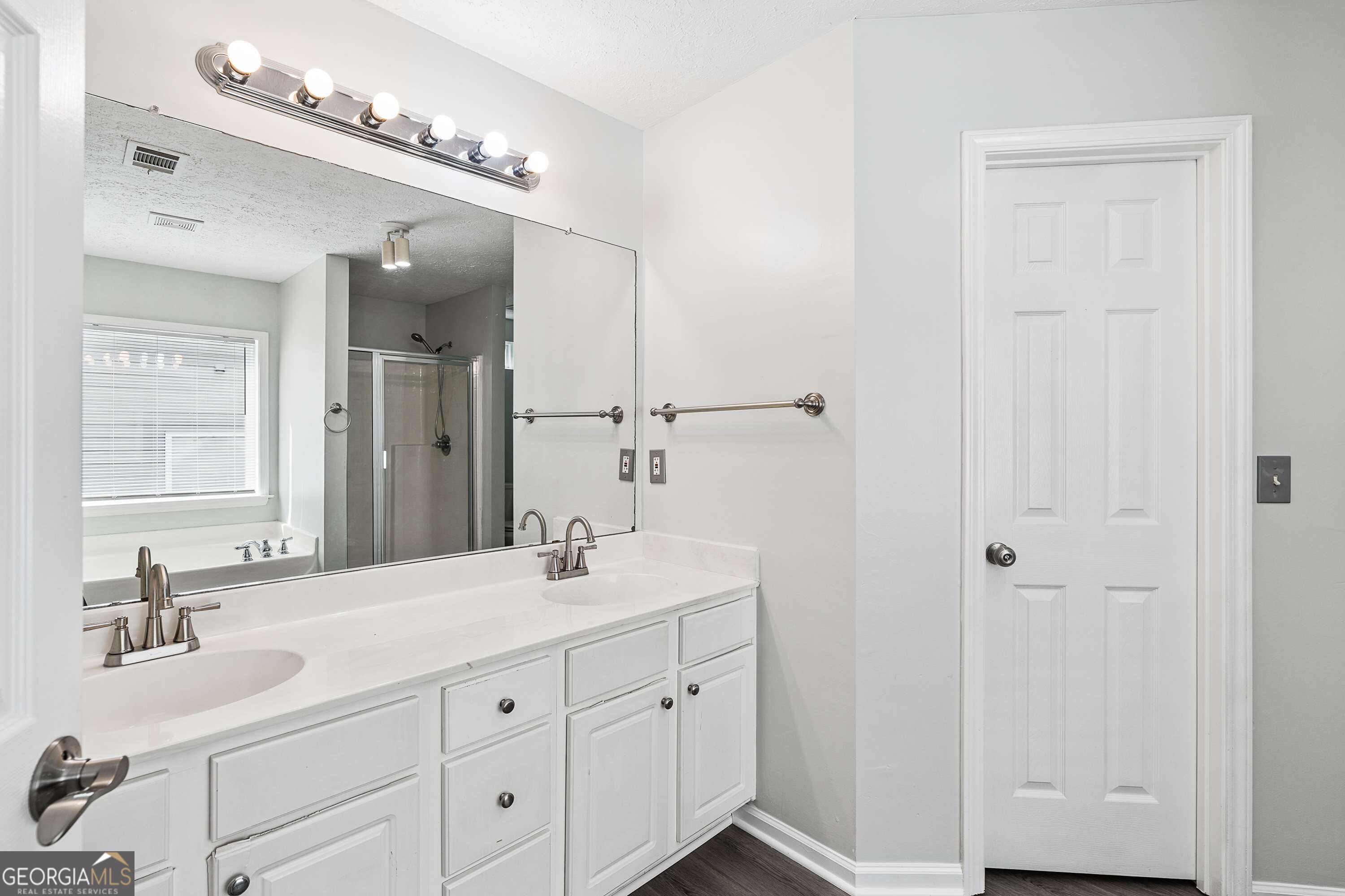 Bathroom with a double-sink white vanity, large mirror, and a glass-enclosed shower reflected in the mirror.