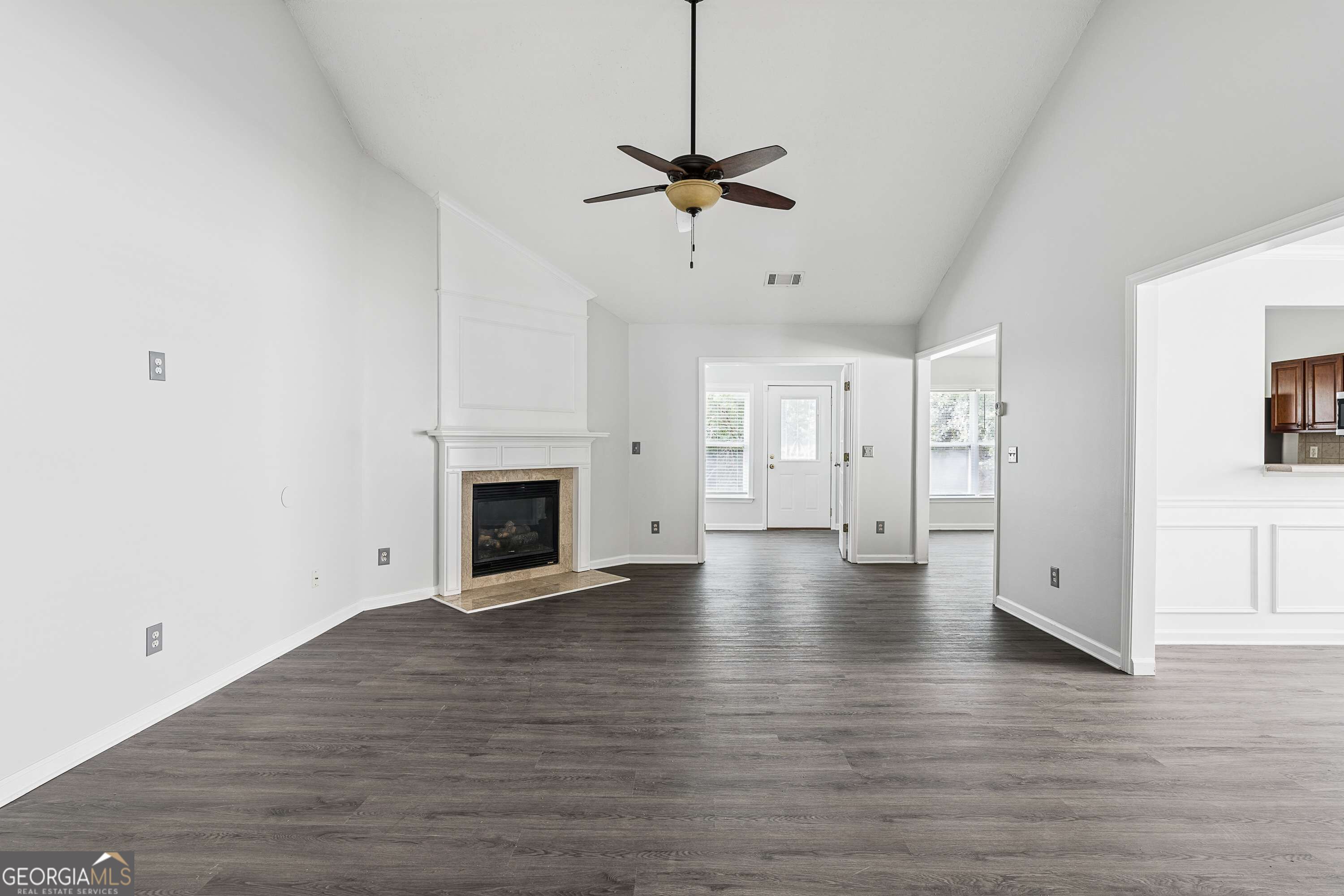 Vacant living room with a white fireplace, dark flooring, and a ceiling fan.