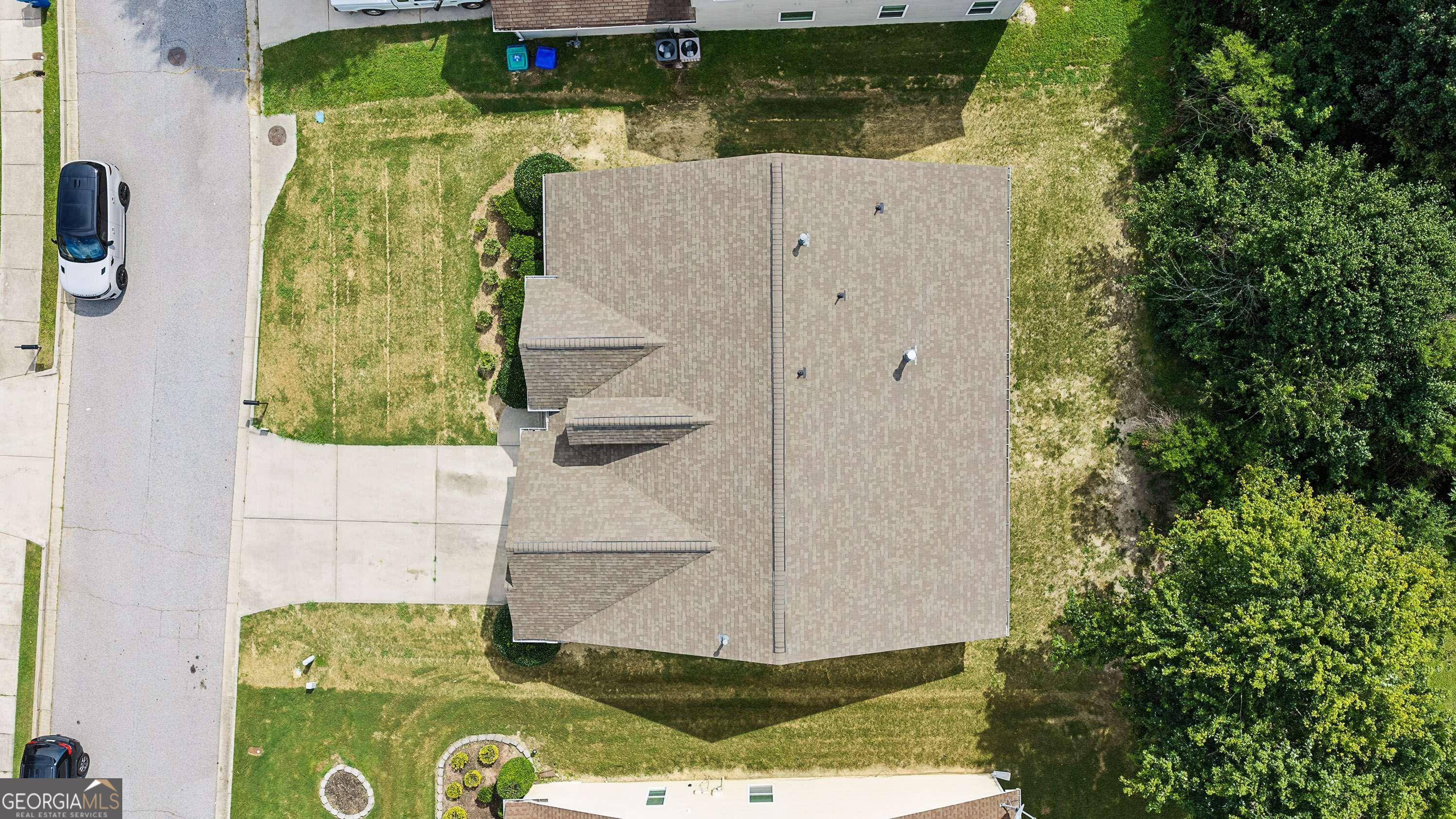 Aerial view of a house’s shingle roof, surrounding lawn, driveway, and mature trees.
