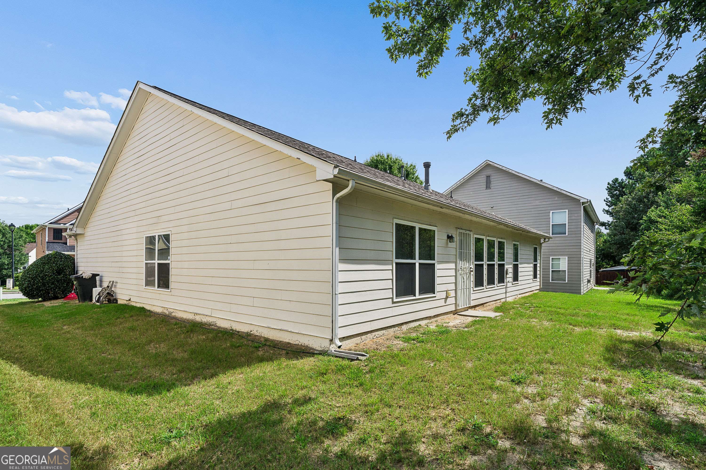 Rear and side of a light-sided house with many windows and a grassy yard.