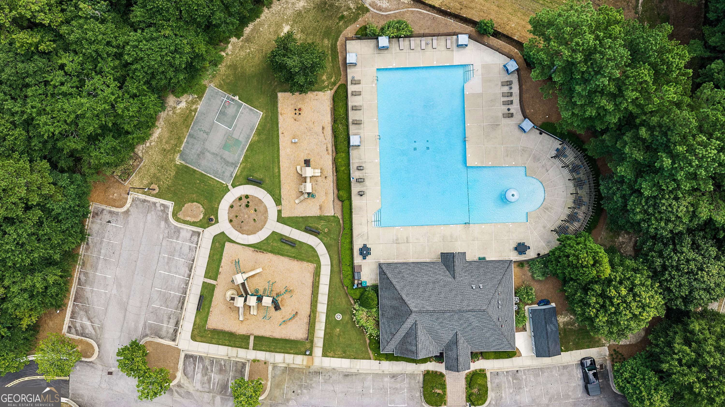 Aerial view of a community pool, playgrounds, sport court, and clubhouse among trees.