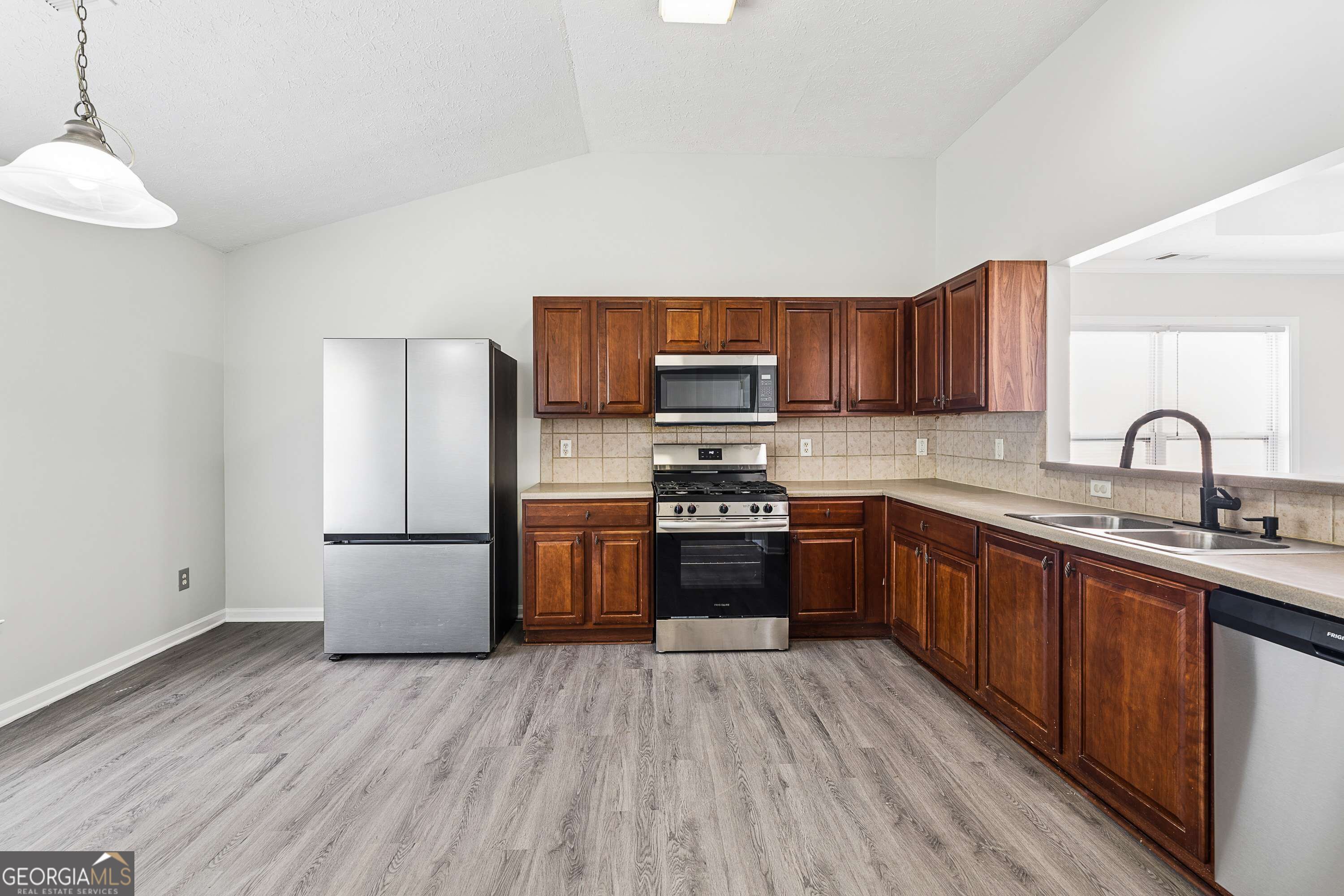 Kitchen with dark wood cabinets, stainless steel appliances, and gray wood-look flooring.