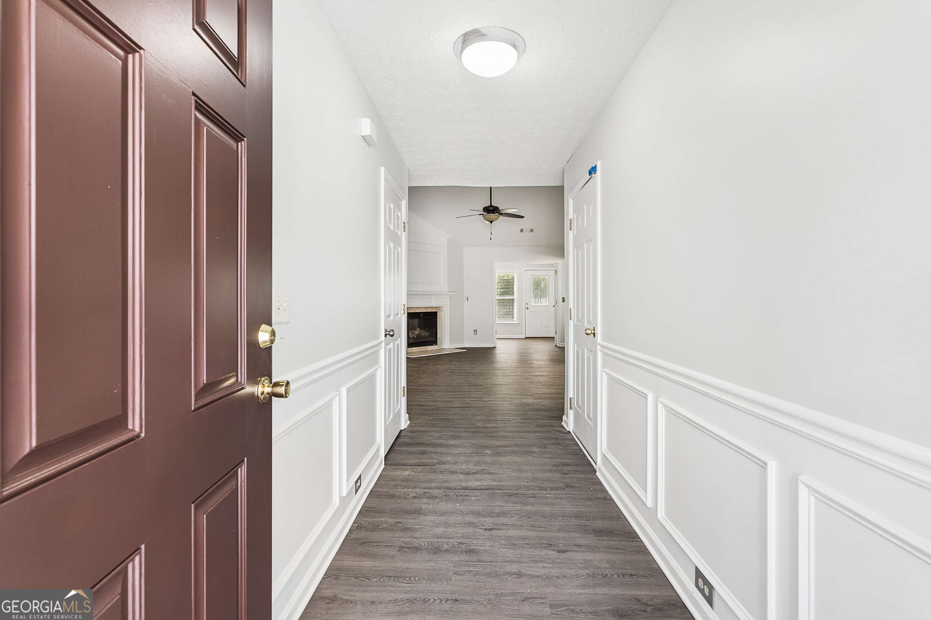 Entry hallway with dark flooring and white wainscoting, opening to a living room with a fireplace.