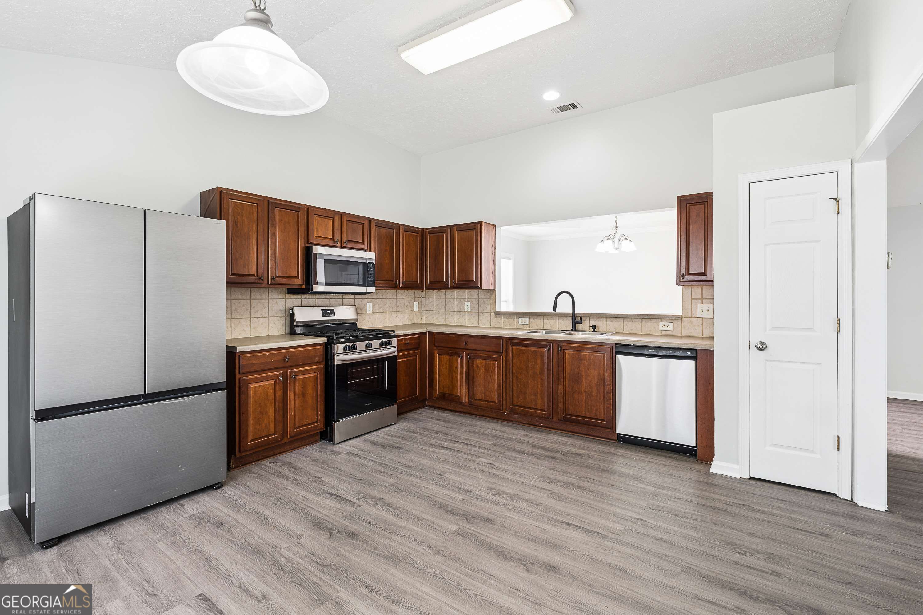 Kitchen with dark wood cabinets, stainless steel appliances, and gray wood-look flooring.