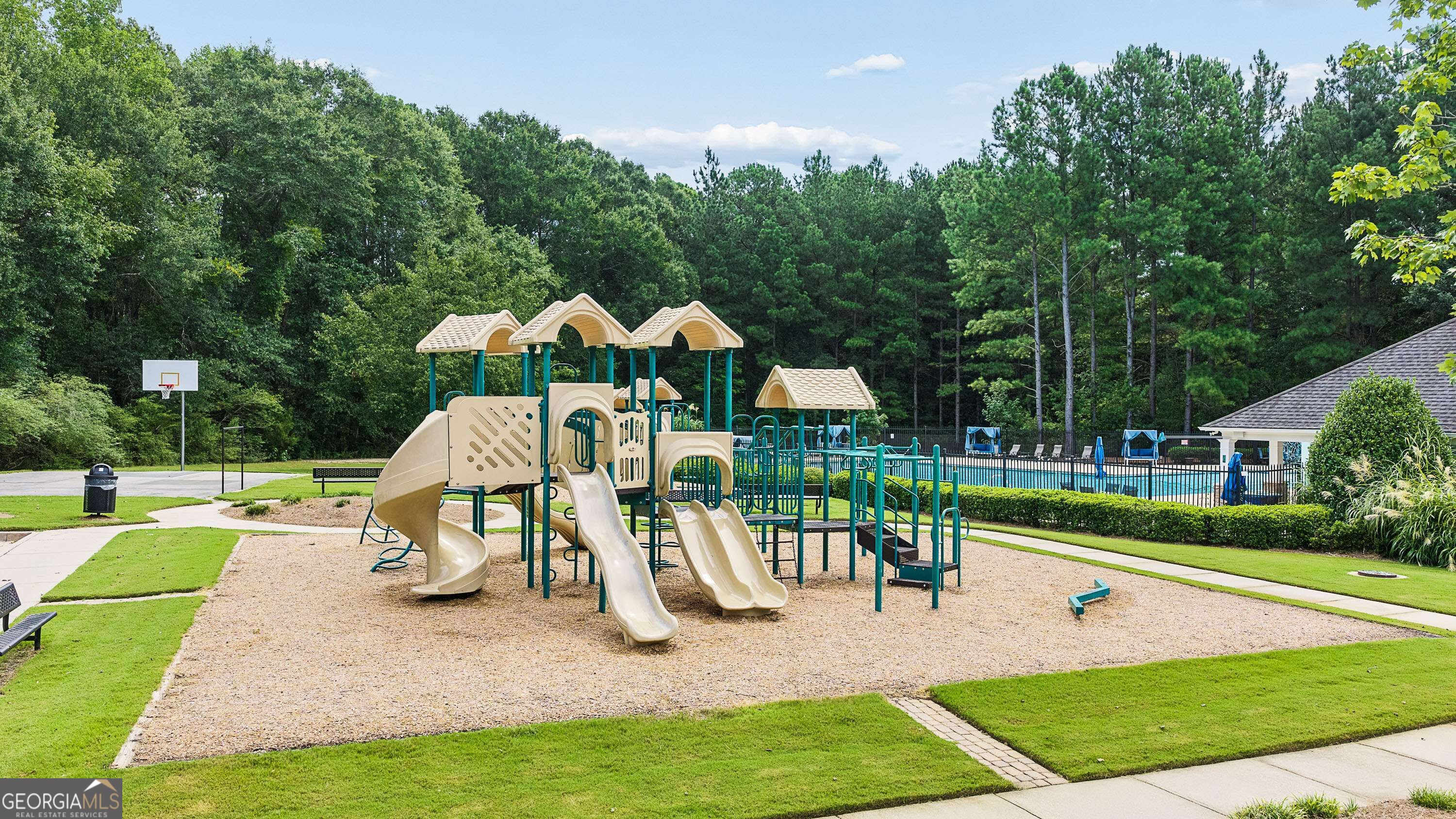 Neighborhood playground with beige slides and teal climbing equipment beside a fenced swimming pool.
