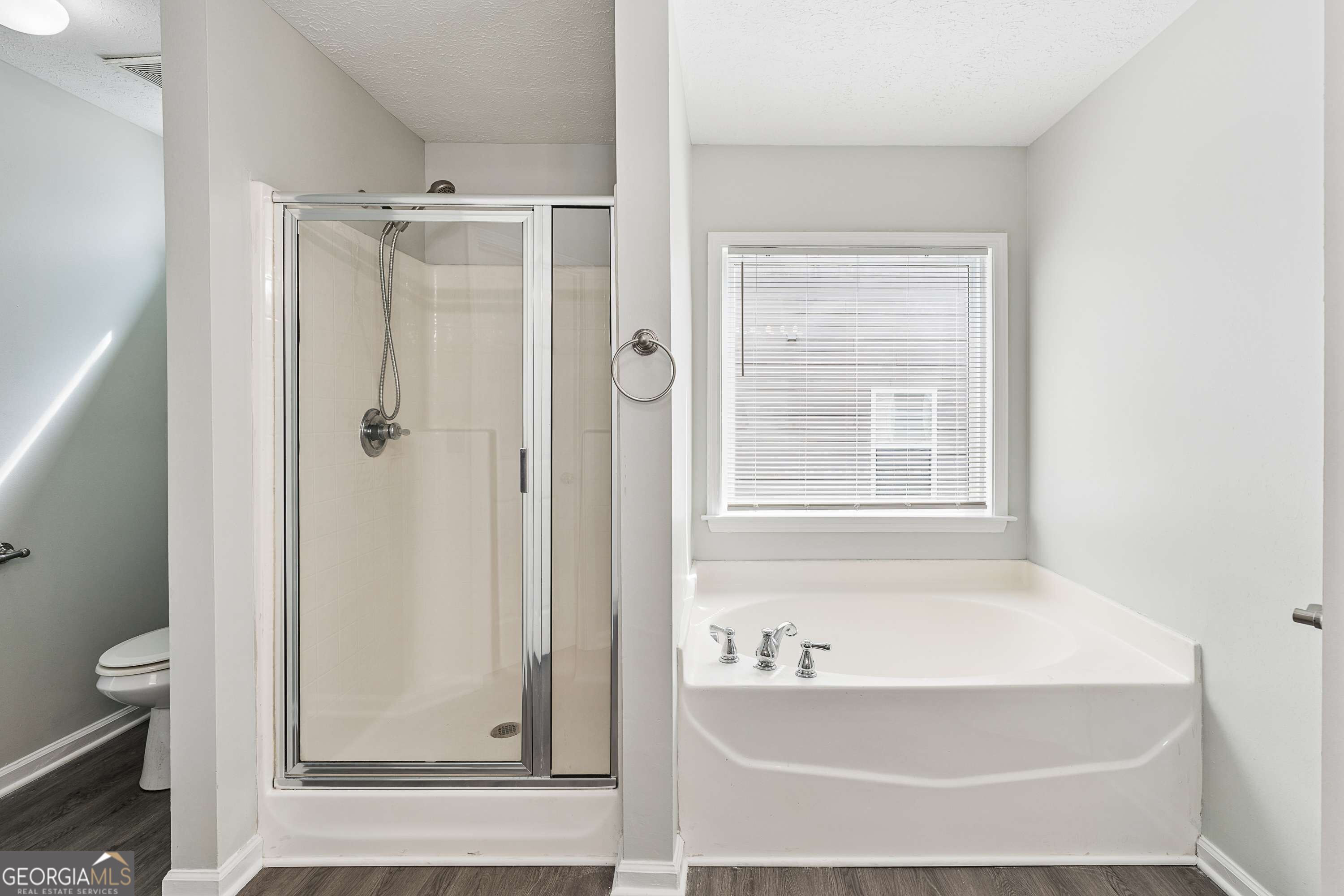 Bathroom with a glass-enclosed shower beside a corner soaking tub and window with blinds.