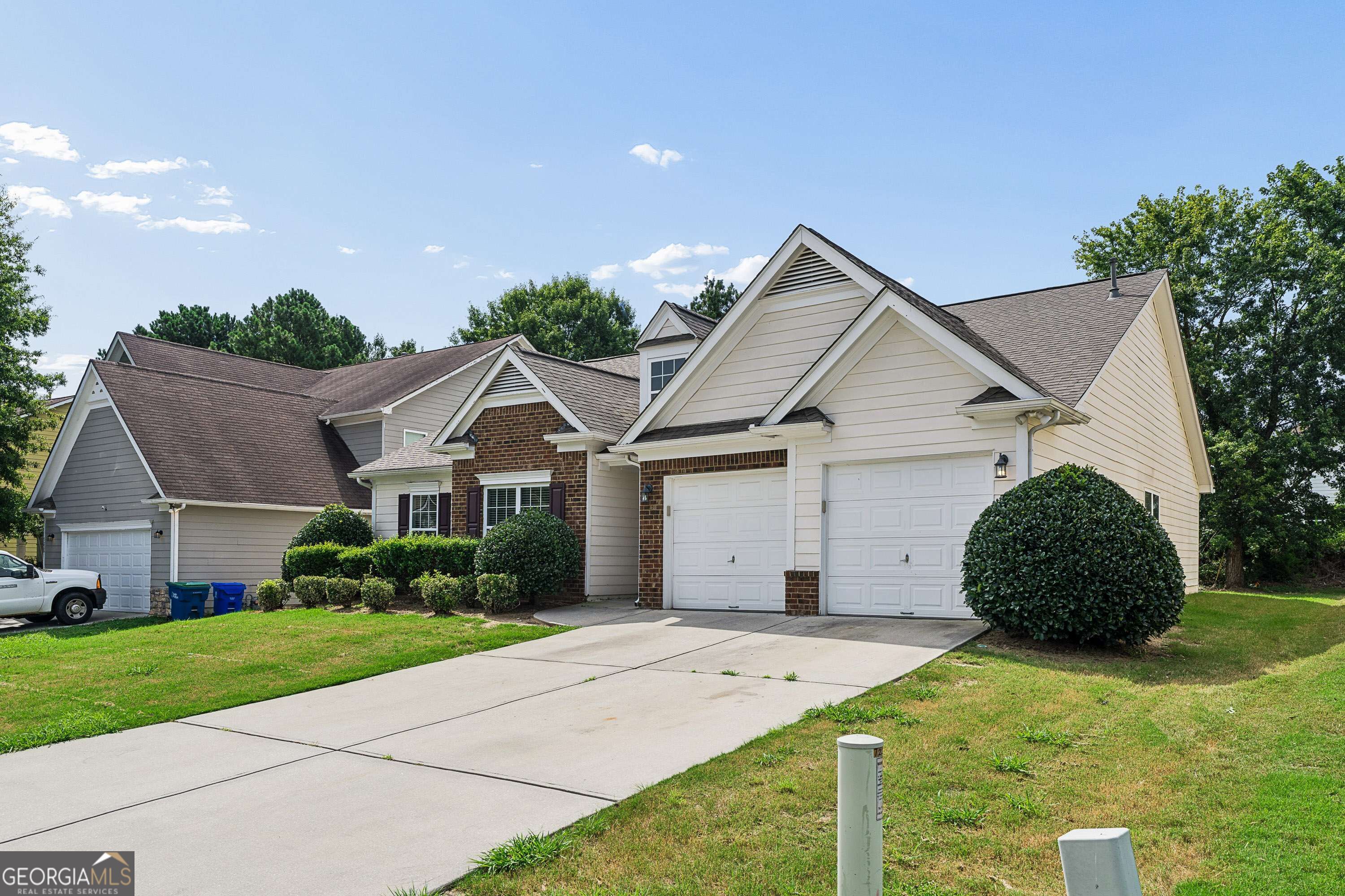 Large light-sided home with brick accents, multiple white garage doors, and a broad concrete driveway.