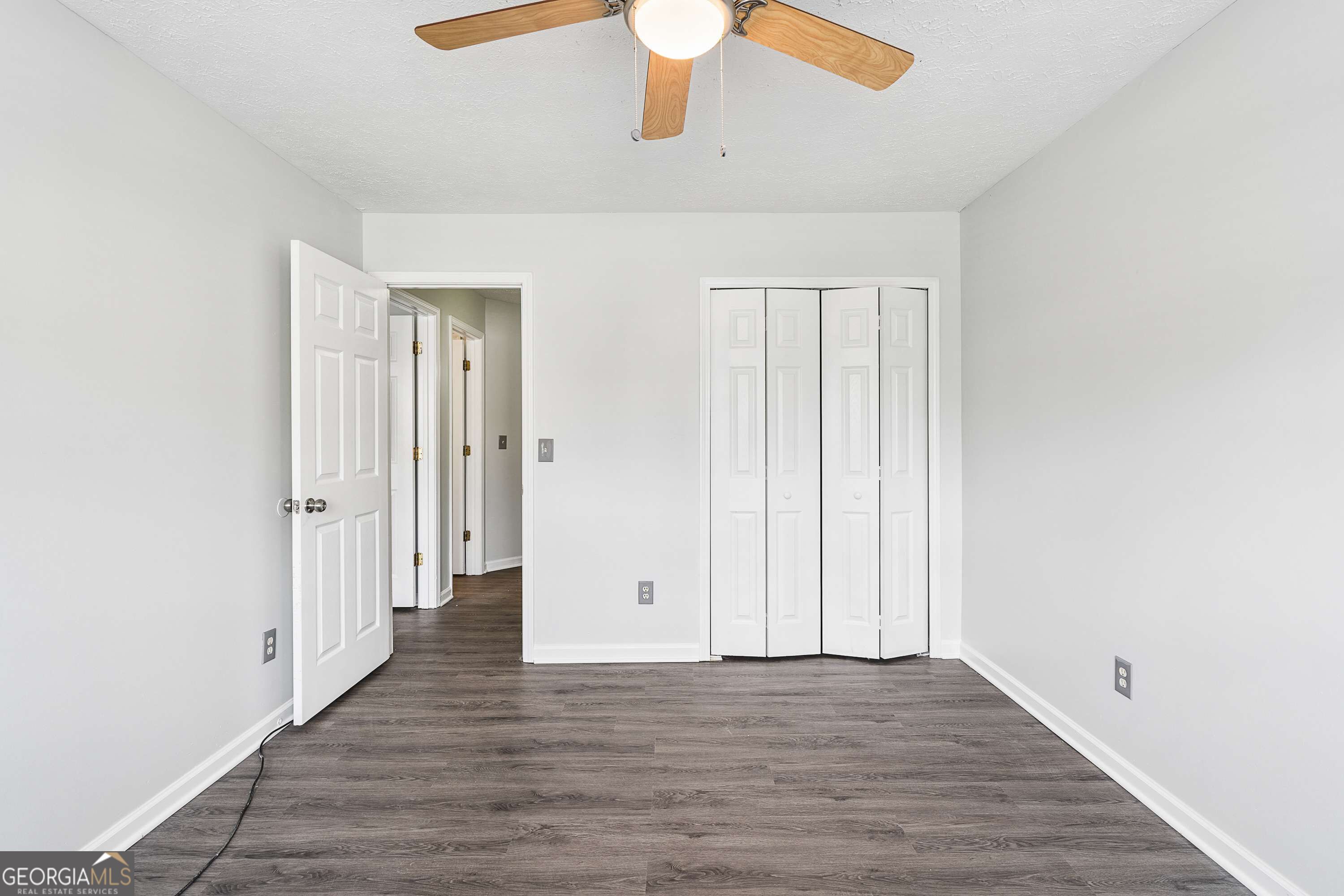 Vacant bedroom with gray wood-look flooring, a ceiling fan, and a folding-door closet.