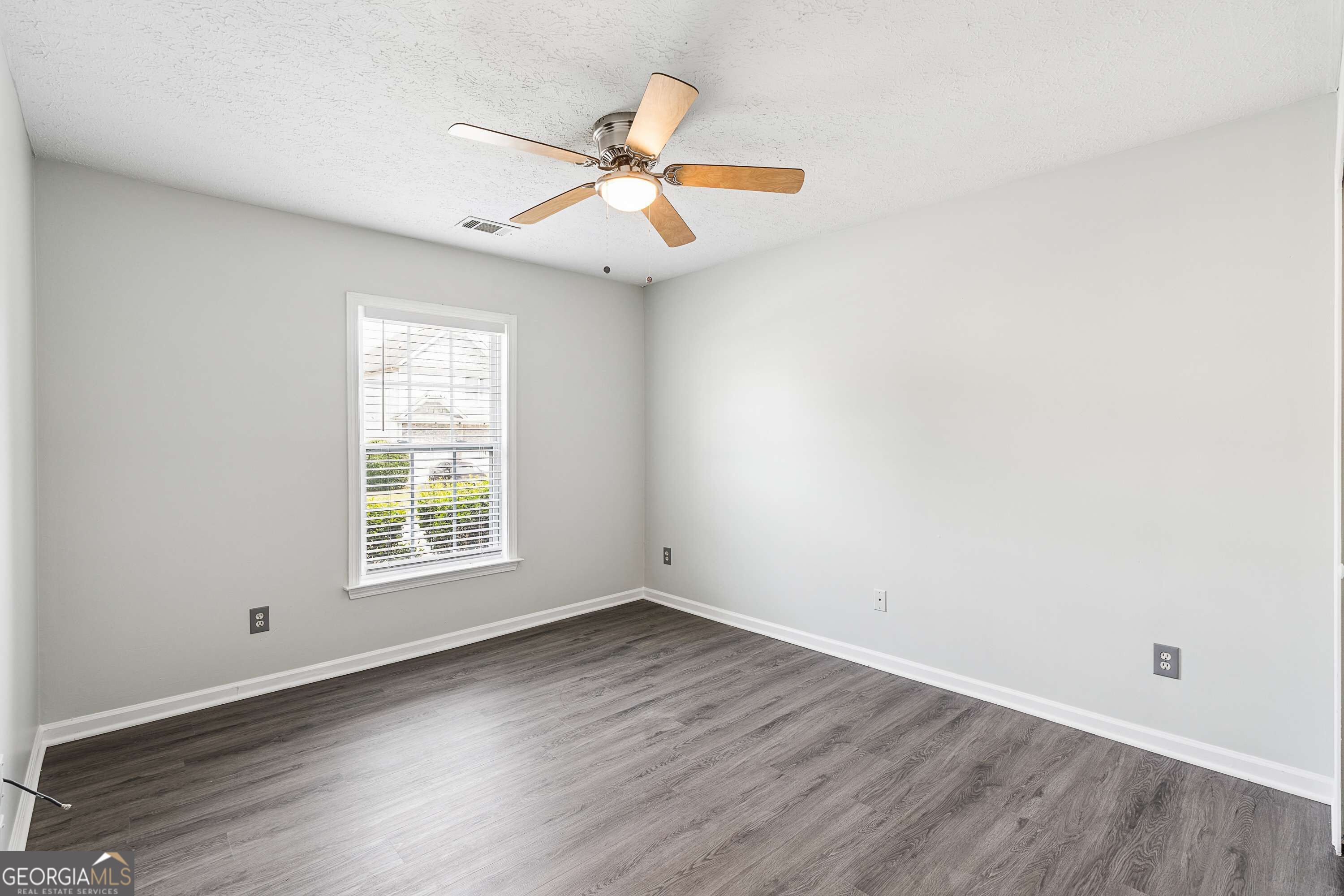 Empty room with gray wood-look flooring, a window with blinds, and a wood-blade ceiling fan.