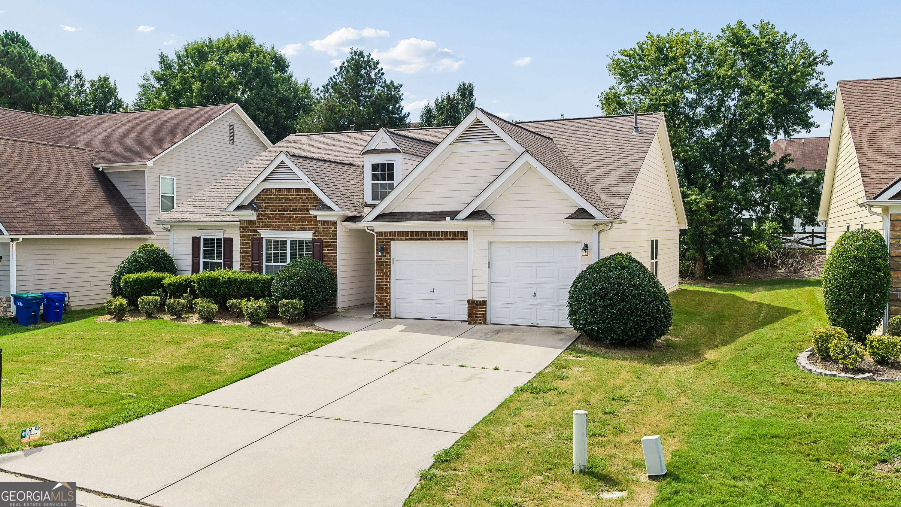 Two-story house with brick accents, two garage doors, a wide driveway, and trimmed shrubs.