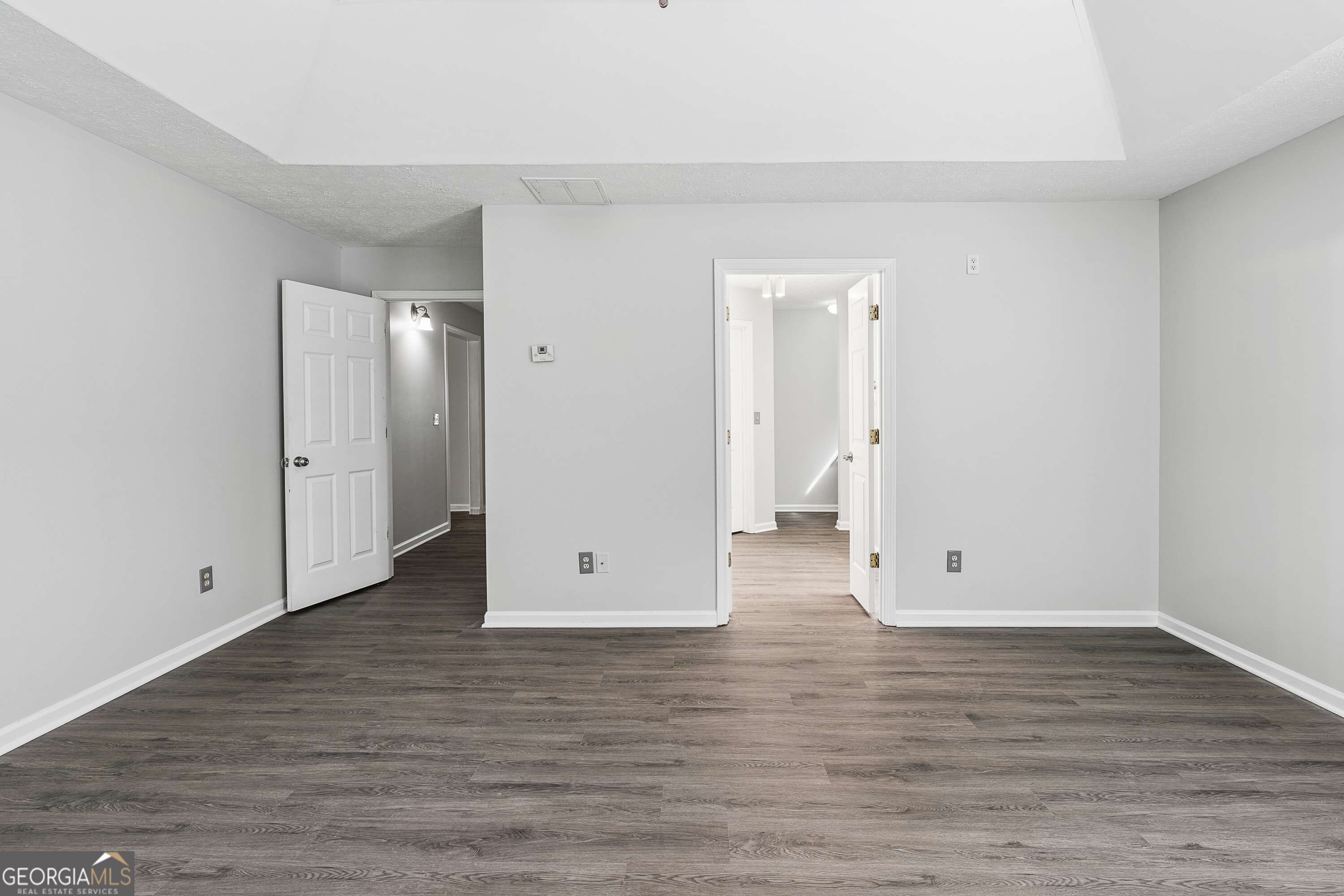 Empty room with dark plank flooring and open doorways to adjoining rooms.