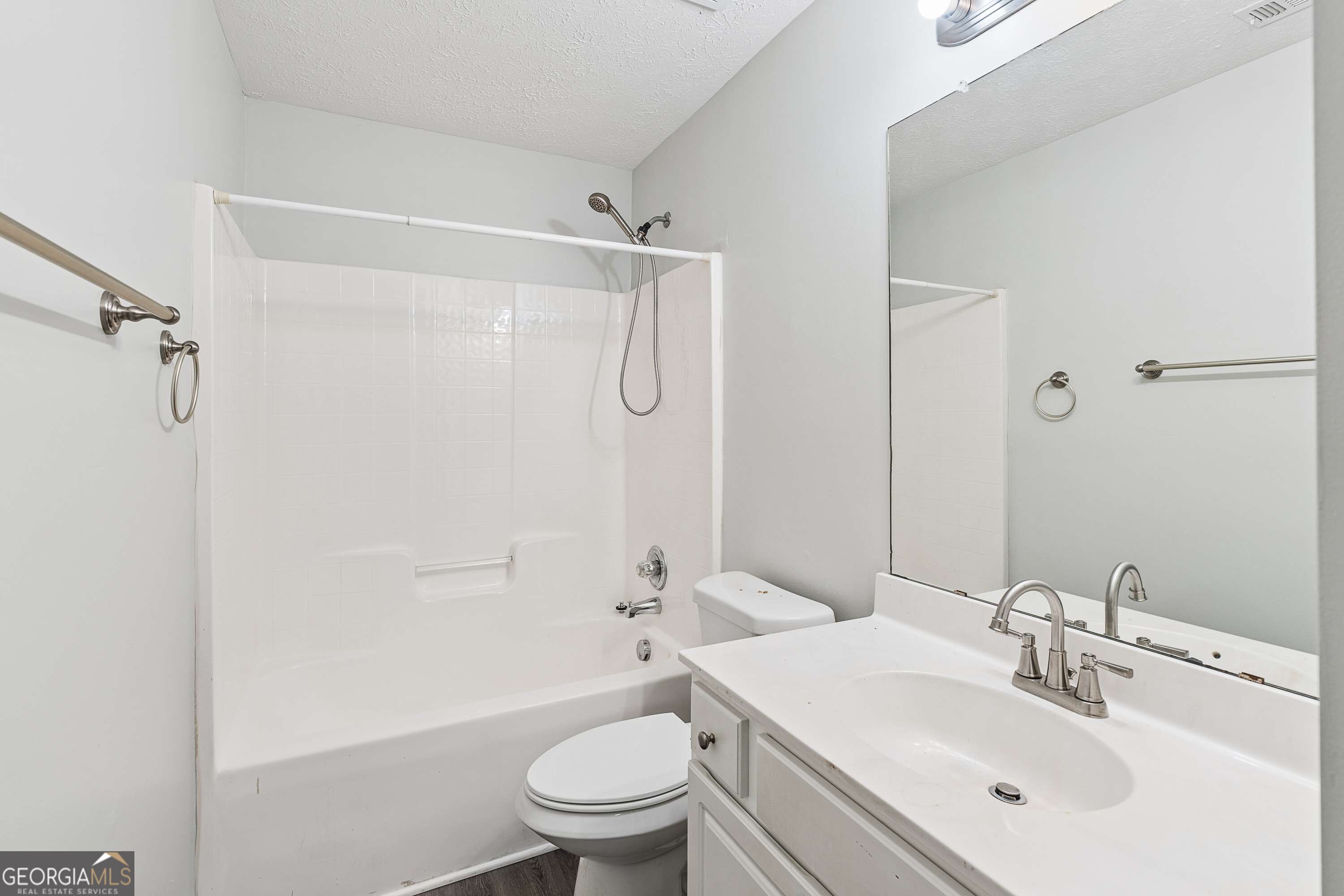 Bathroom with a white tub-shower combination, toilet, and vanity with a large mirror.