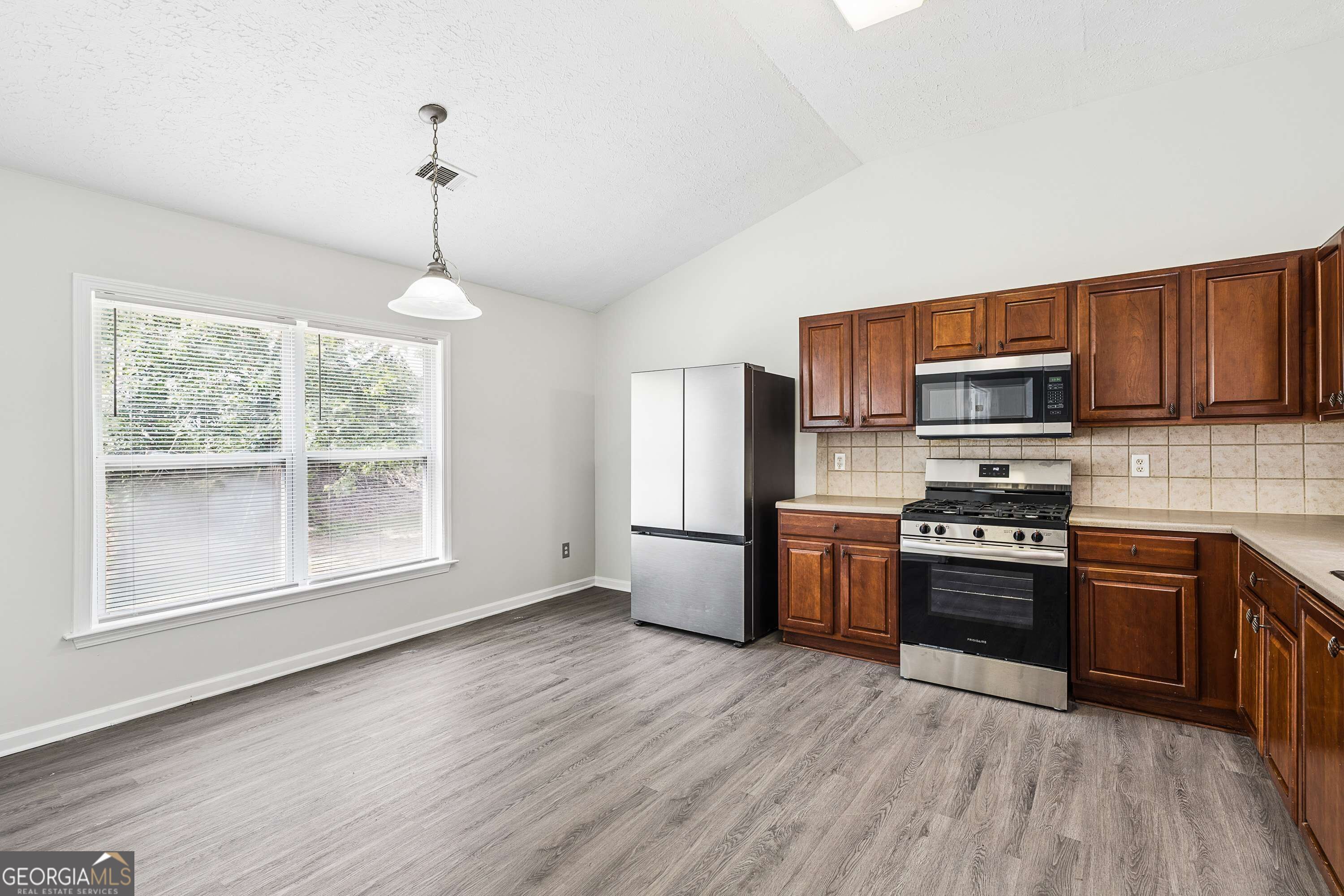 Vacant kitchen with dark wood cabinets, stainless steel appliances, and gray plank flooring.