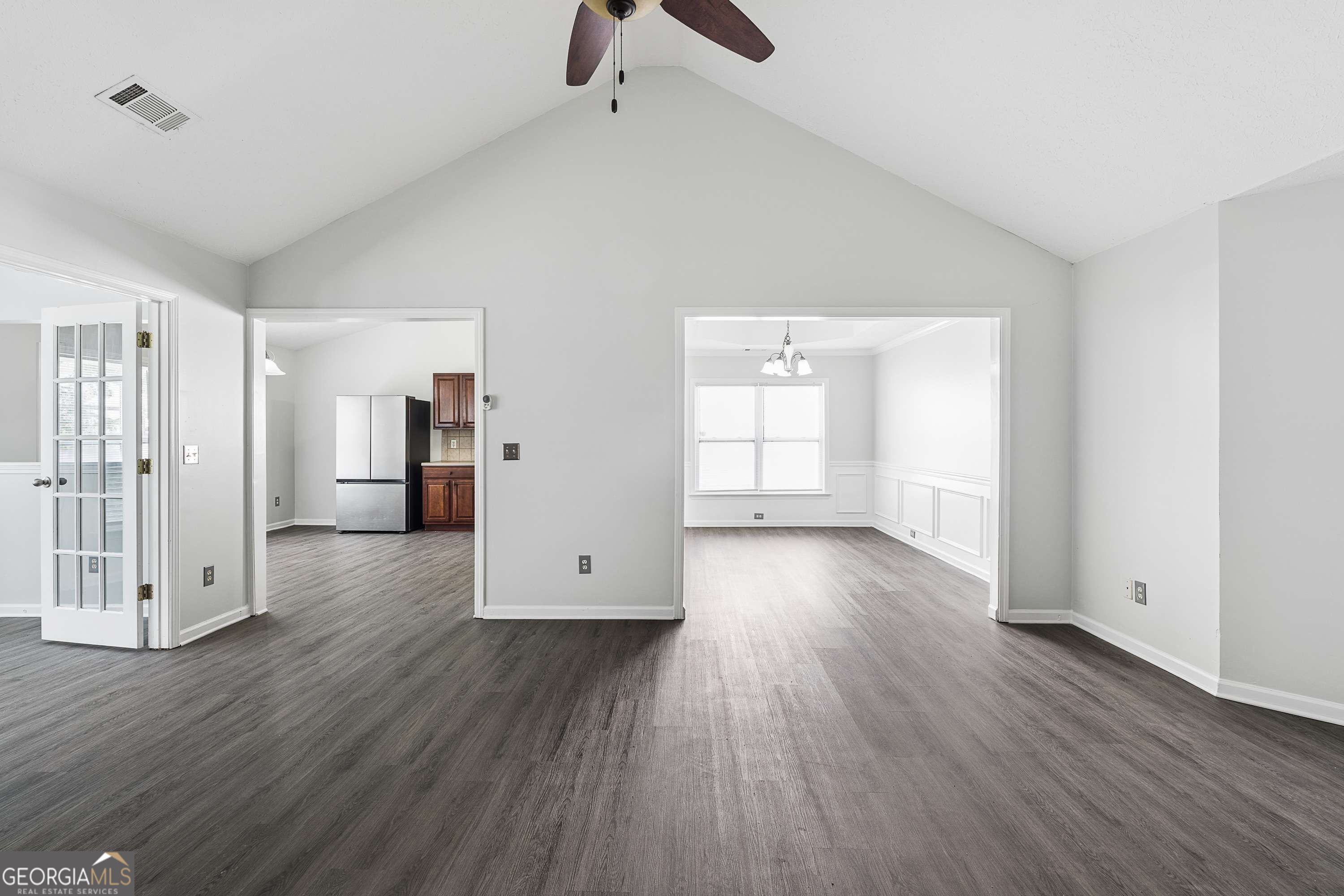 Vacant living room with vaulted ceiling, dark flooring, ceiling fan, and wide openings to adjoining rooms.