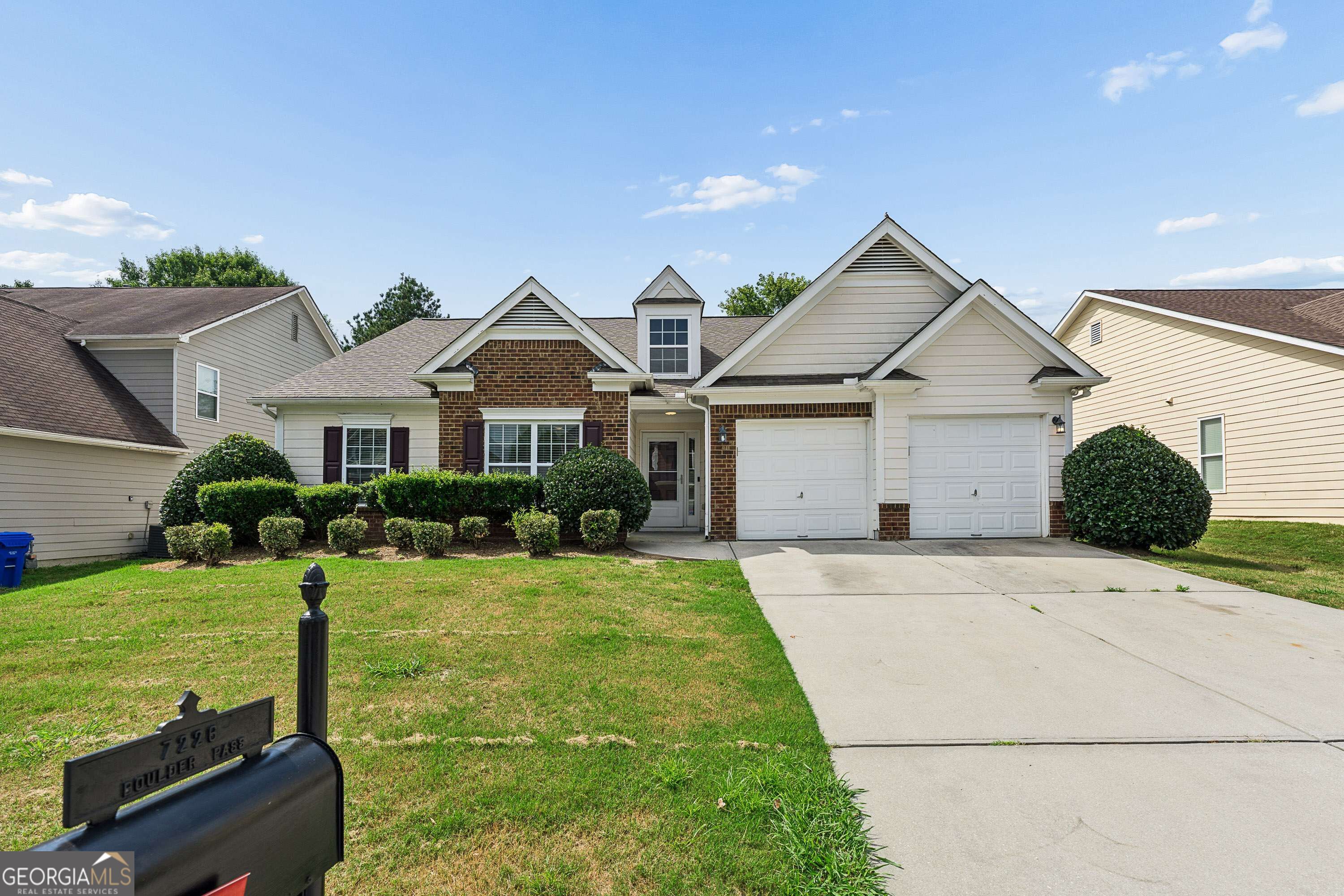 Suburban home with brick accents, white siding, and two garage doors, viewed from the front driveway.