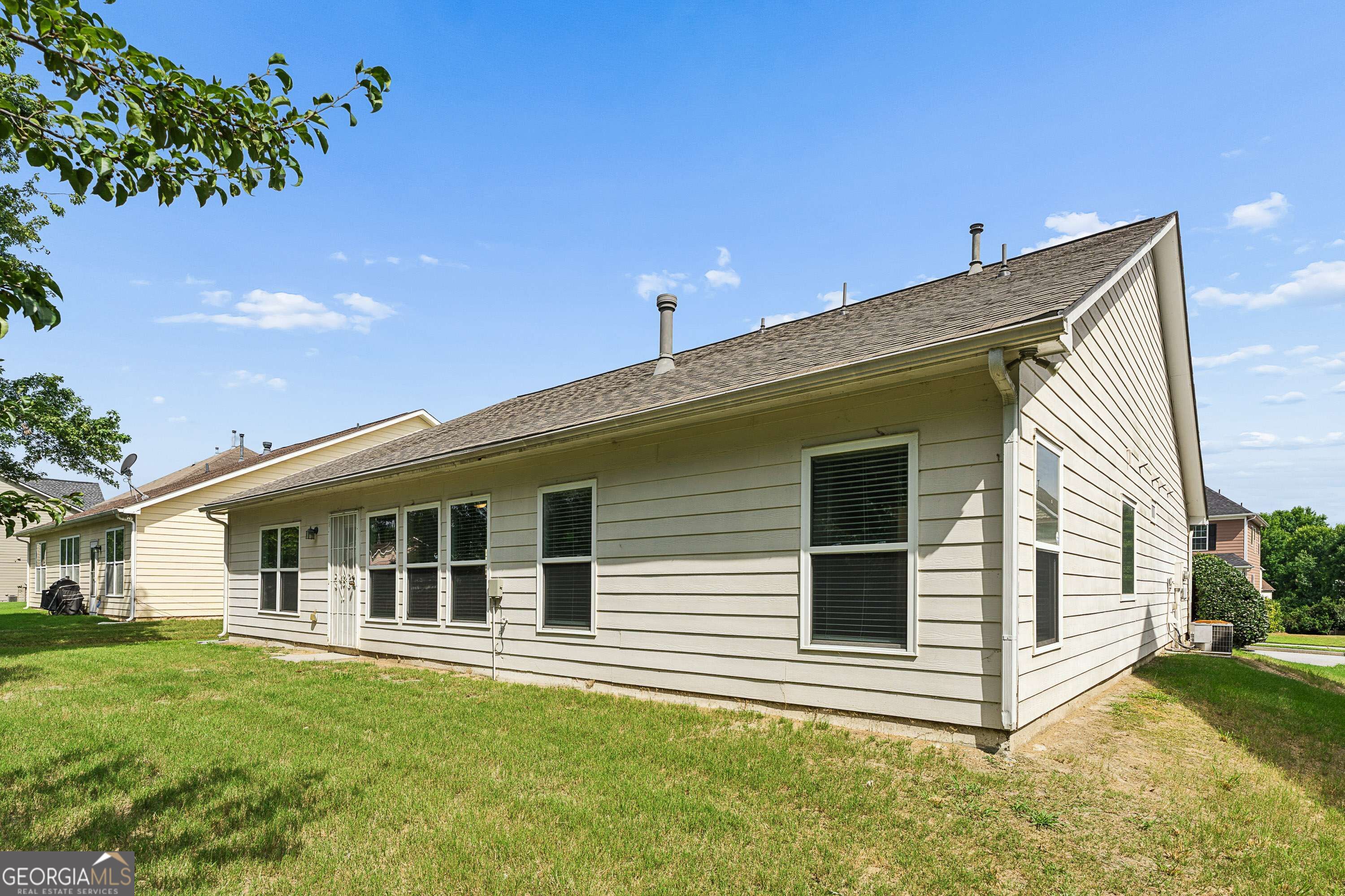 Rear and side of a light-sided house with multiple windows and a grassy yard.