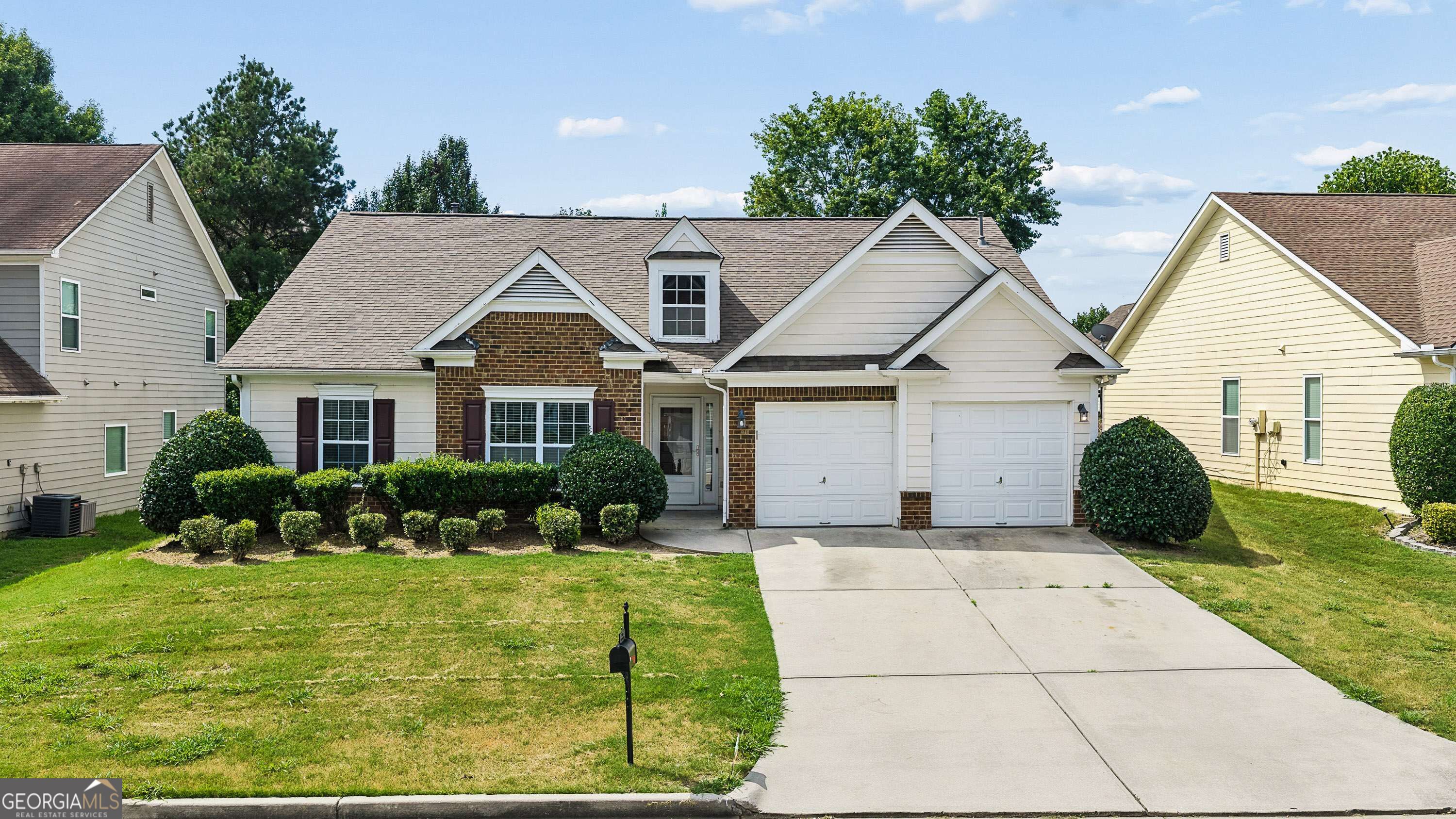 Two-story house with brick facade, double garage, broad driveway, and neatly trimmed front shrubs.