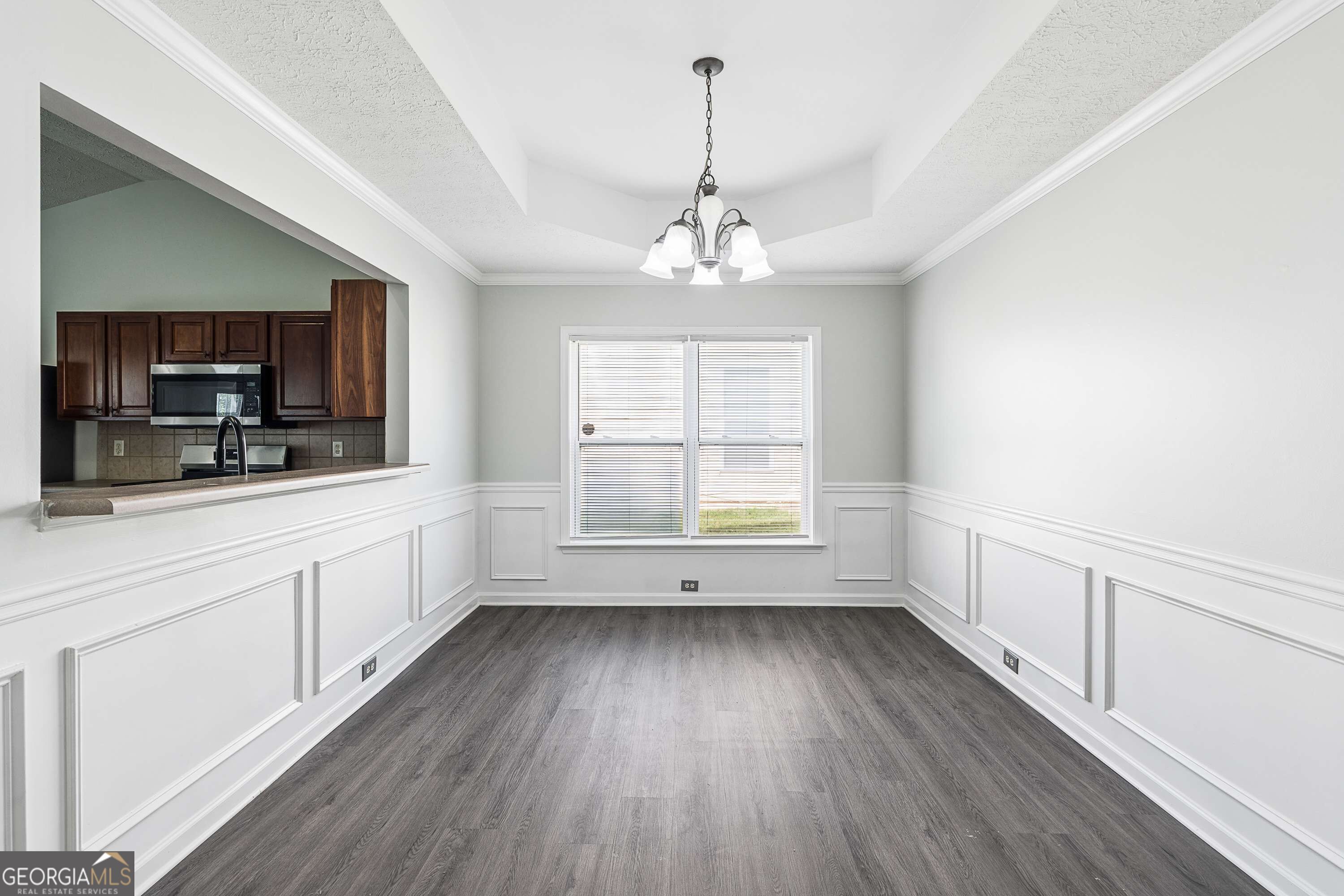 Vacant dining area with paneled wainscoting, a tray ceiling, and a pass-through to the kitchen.