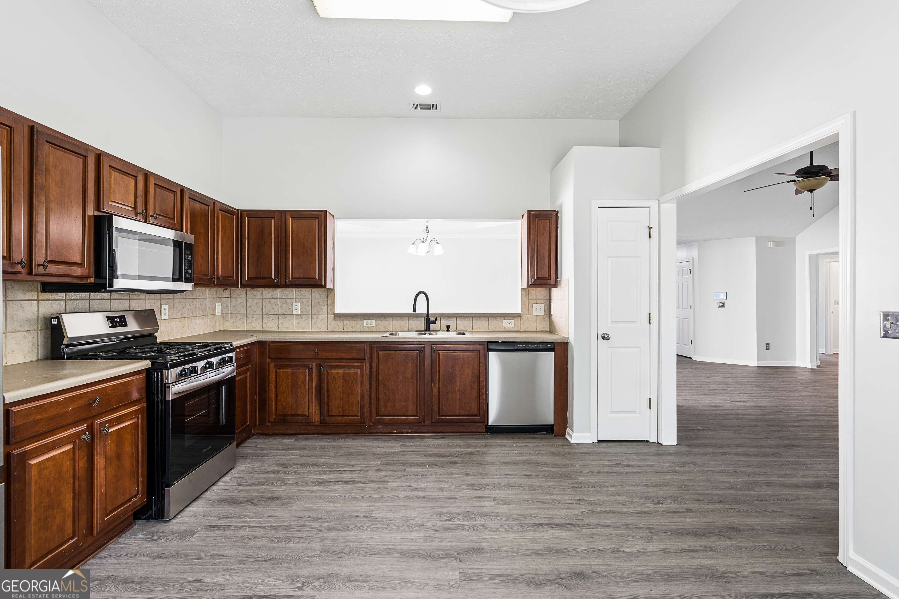 Kitchen with dark wood cabinets, stainless steel appliances, and gray wood-look flooring.