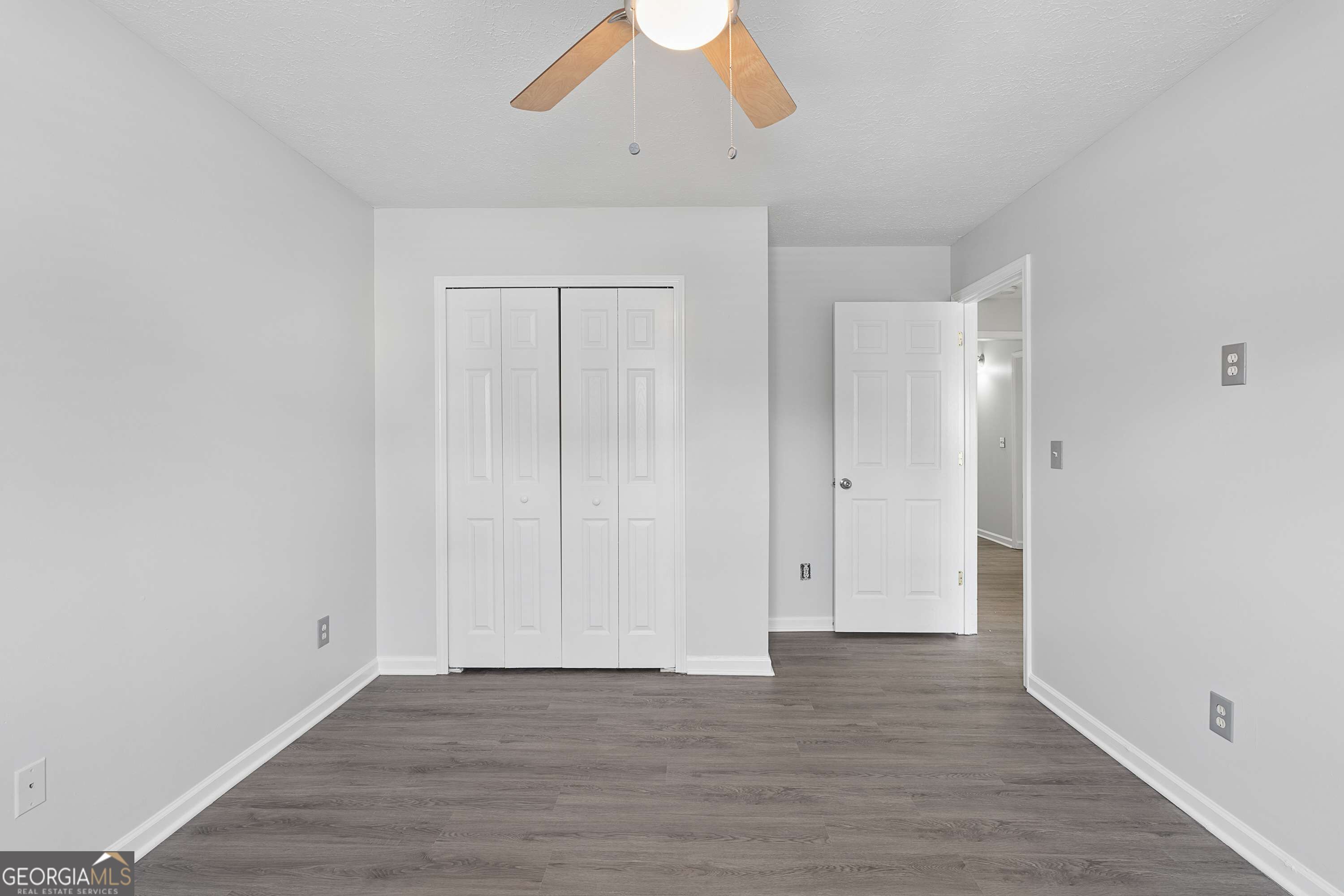 Empty bedroom with gray wood-look flooring, a white double-door closet, and a ceiling fan.