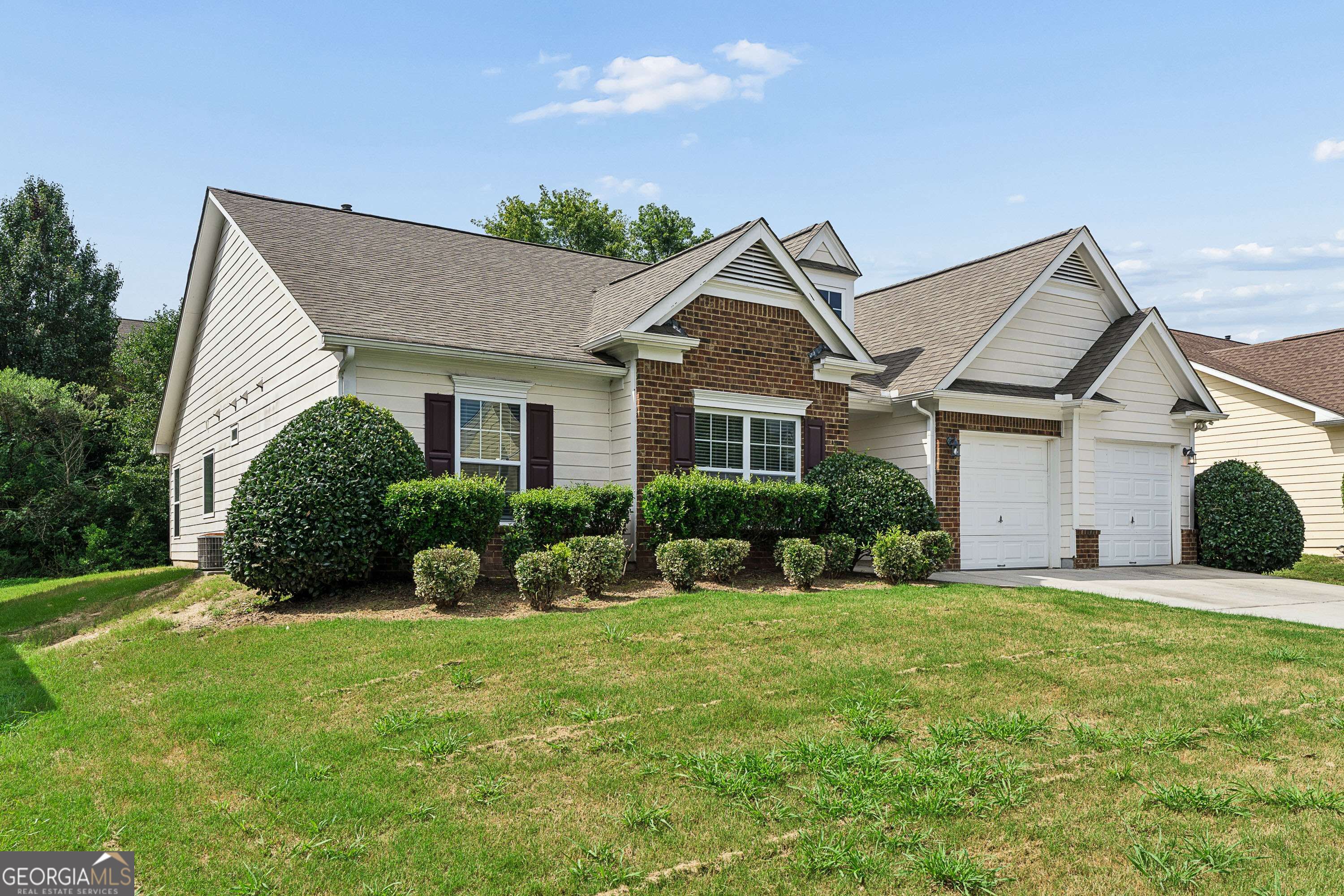 House with cream siding, brick accents, two garage doors, and trimmed shrubs along the front.