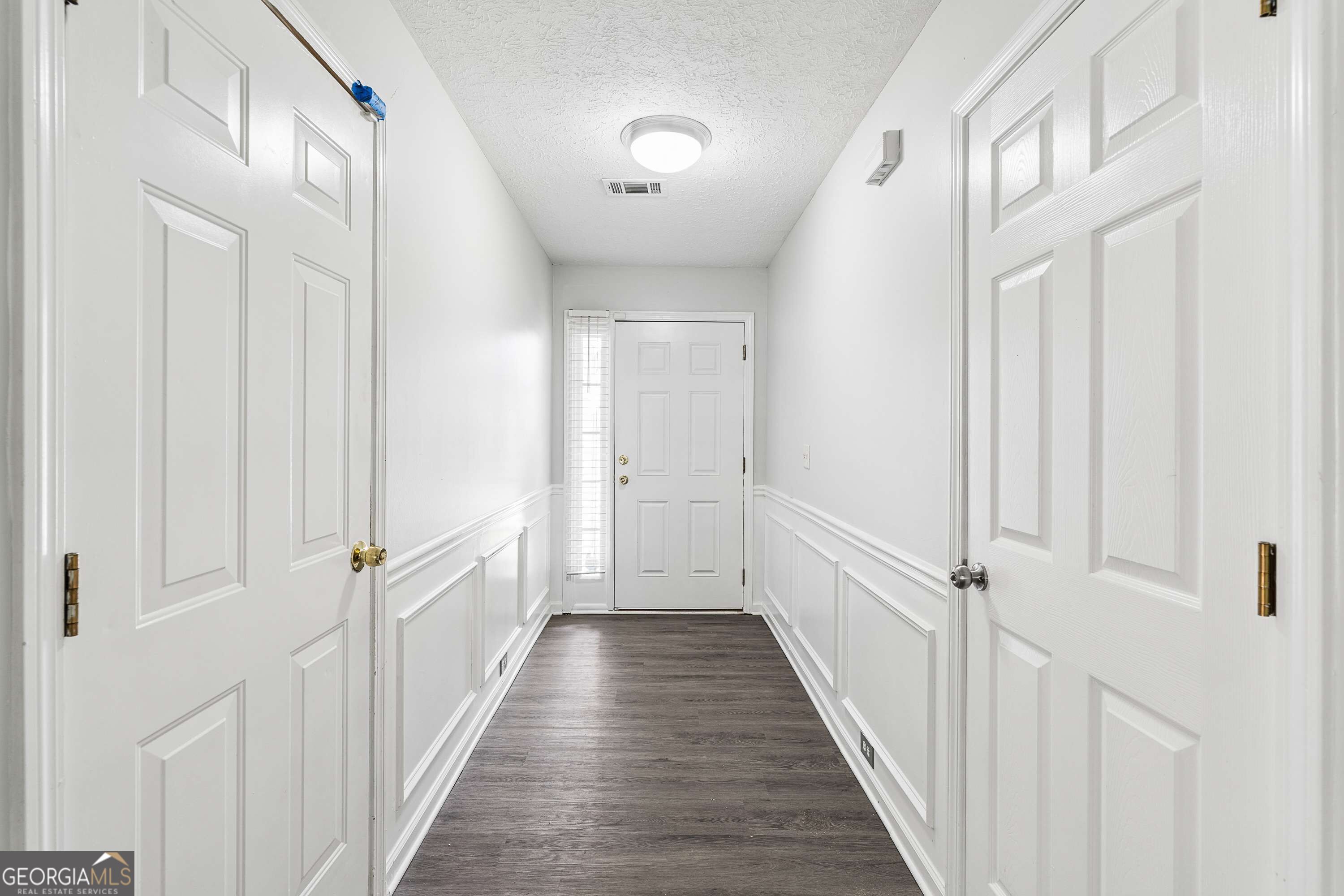 Entry hallway with white paneled walls, dark flooring, and a front door with a slim sidelight.