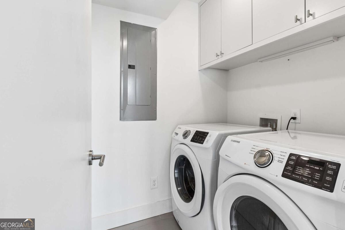 Laundry room with front-loading washer and dryer beneath white cabinets.
