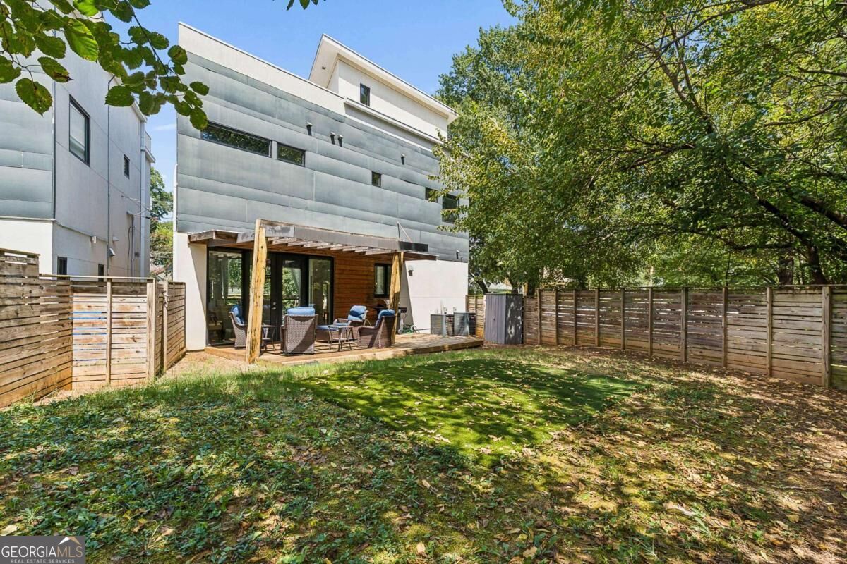Modern home’s rear patio and fenced backyard shaded by mature trees.