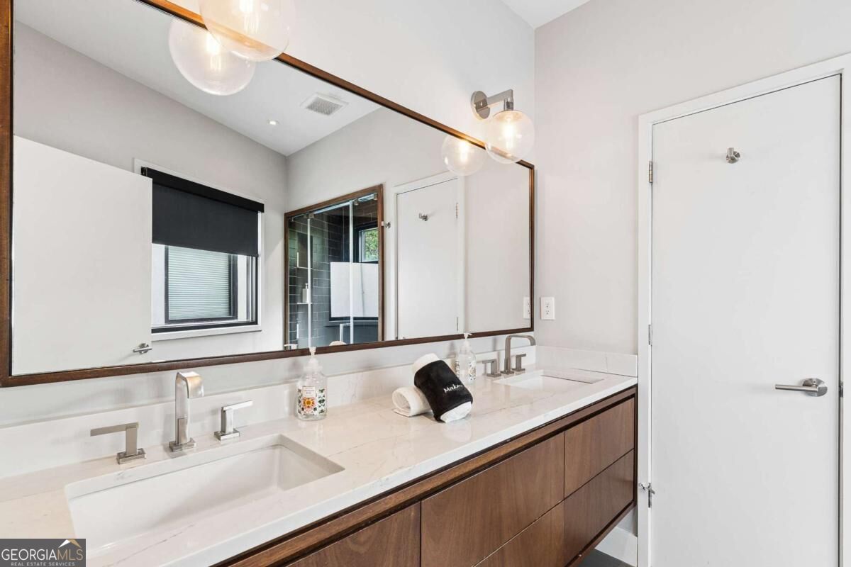 Bathroom vanity with a white countertop, wood cabinetry, and a wide framed mirror.