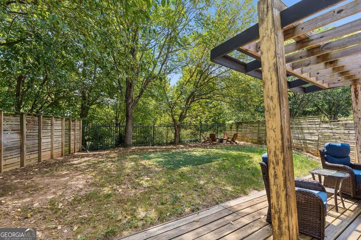 Fenced backyard with a pergola-covered deck, patio seating, and a patch of artificial turf.