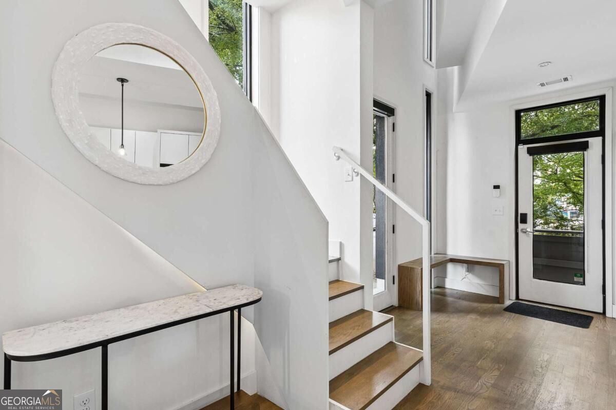 Modern entryway with a white staircase, round mirror, slim console table, and glass-paneled front door.
