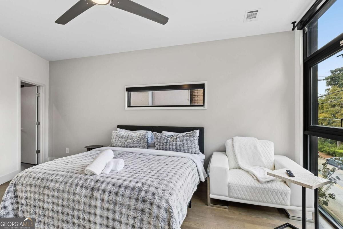 Furnished bedroom with a large bed, white armchair, and floor-to-ceiling windows.