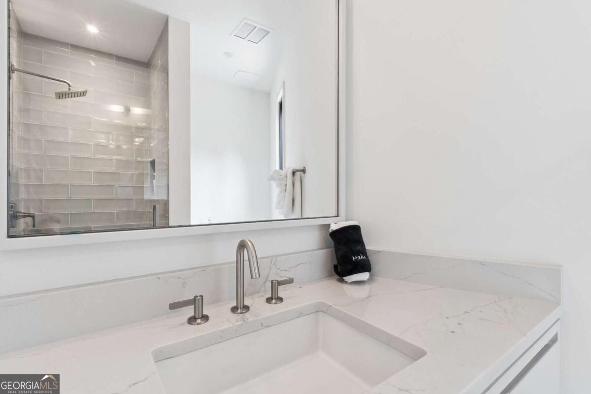Bathroom vanity with a marble-look counter, brushed metal faucet, and mirror reflecting a tiled shower.