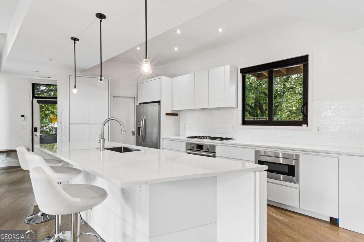 Bright modern kitchen with a large white island, pendant lights, and stainless steel appliances.
