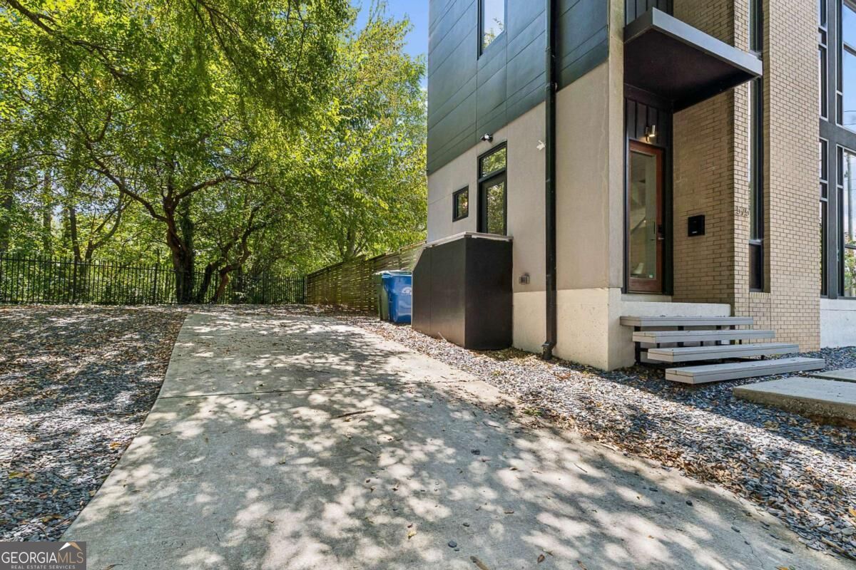 Modern home entrance beside a broad concrete driveway, shaded by leafy trees.