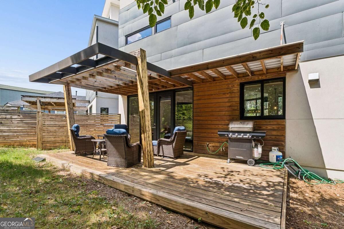 Rear deck with a timber pergola, outdoor seating, and barbecue grill beside a modern home.