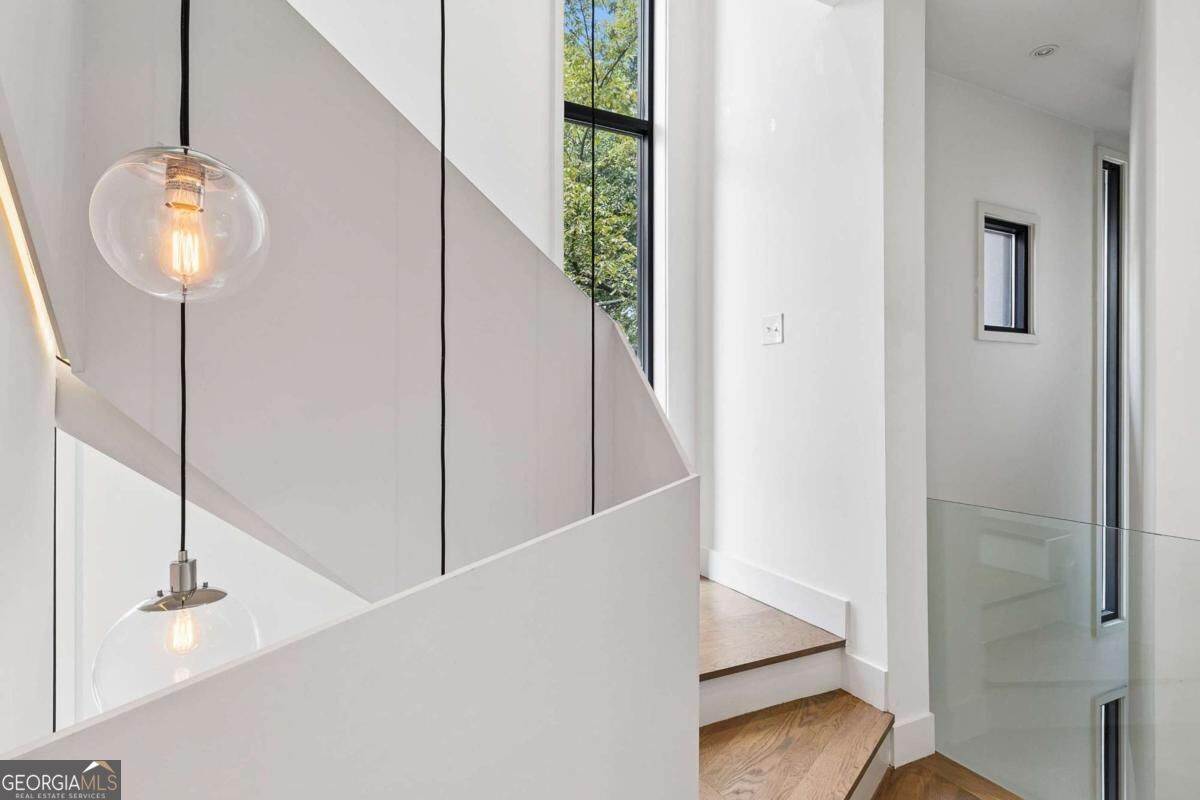 Modern stairwell with wood steps, glass railing, tall windows, and globe pendant lights.