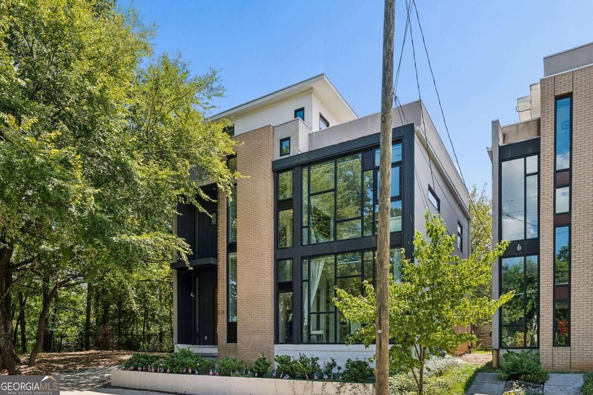 Modern brick home with expansive black-framed windows beside mature trees.