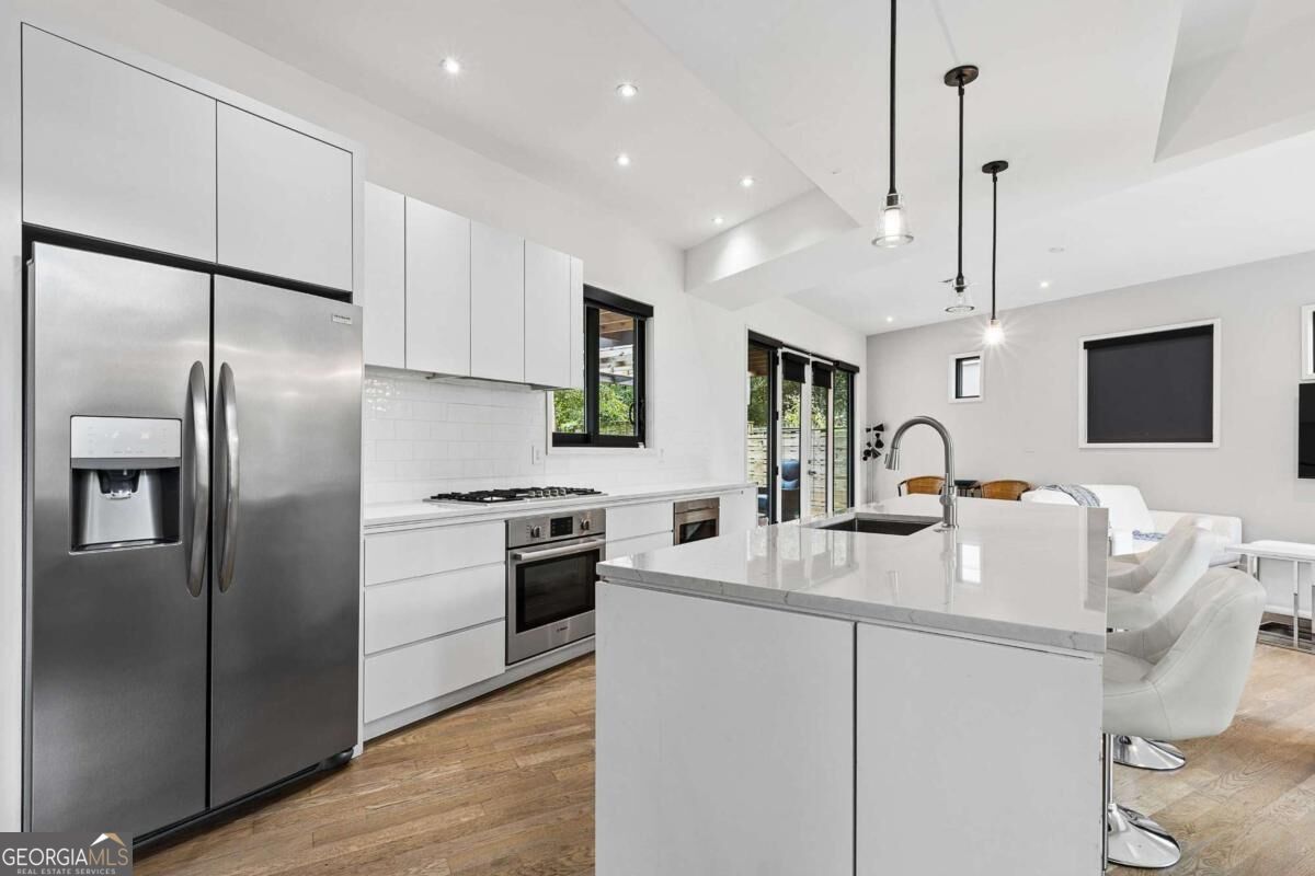 Modern kitchen with a large white island, stainless steel appliances, and an adjoining living area.