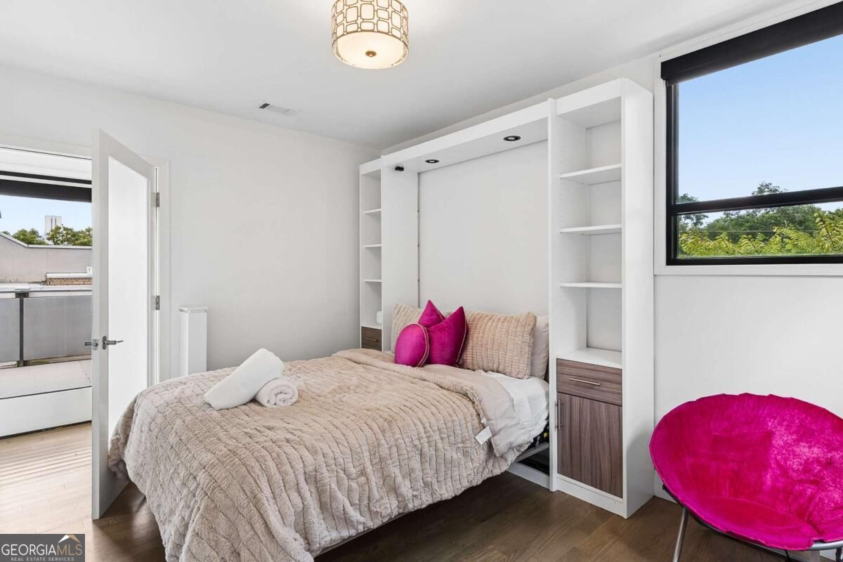 Bedroom with built-in shelving, a quilted bed, and an open balcony door.