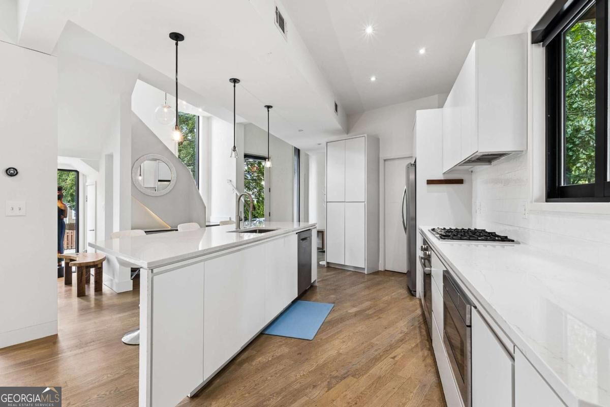 Modern white kitchen with a large island, quartz counters, gas cooktop, and warm wood floors.