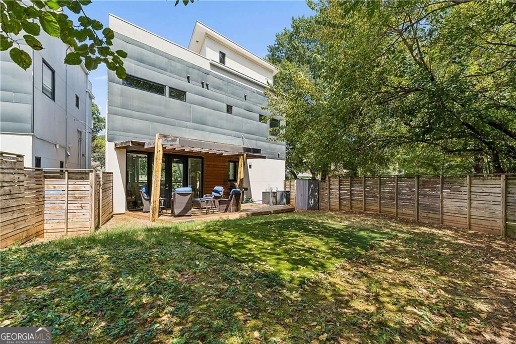 Modern home’s rear patio and enclosed yard, with outdoor seating, wood fencing, and mature trees.