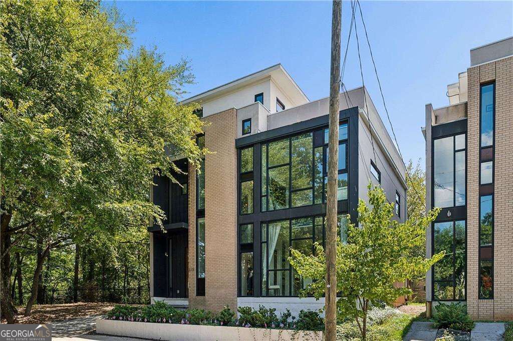 Modern brick residence with large black-framed windows, landscaped beds, and mature trees.