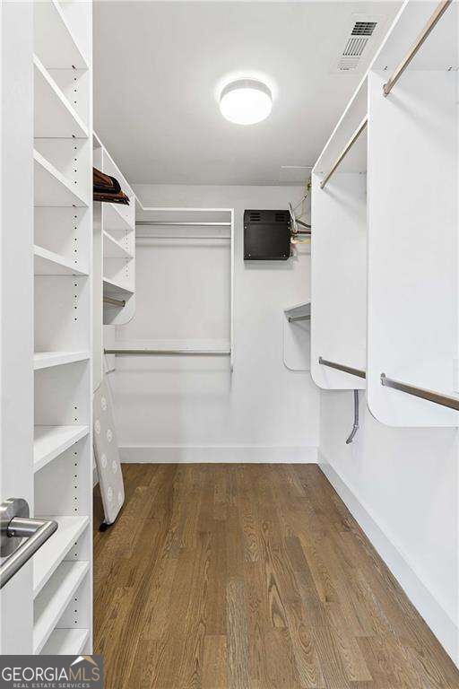 Walk-in closet with built-in white shelving, hanging rods, and wood flooring.
