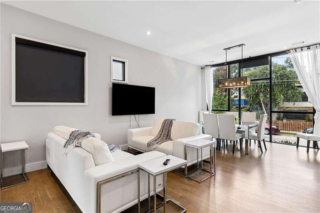 Open-plan living and dining room with white sofas, hardwood floors, and large street-facing windows.