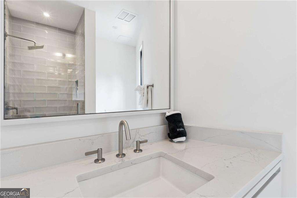 Bathroom vanity with a veined quartz counter, undermount sink, modern faucet, and mirror reflecting a tiled shower.