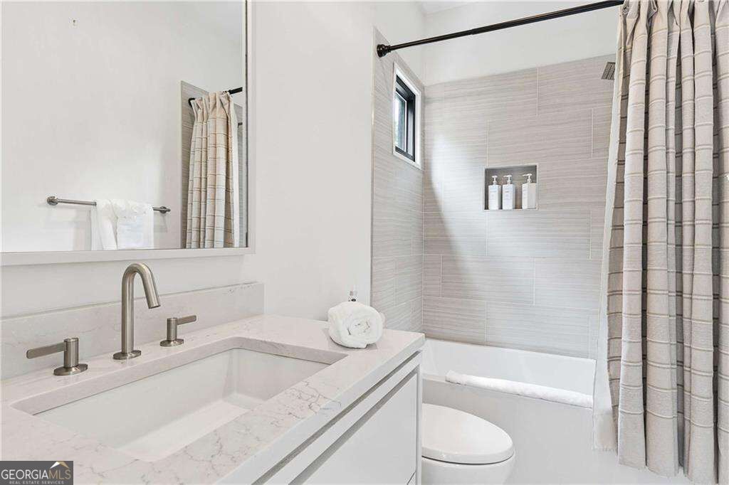 Bathroom with a marble-look vanity, undermount sink, and tiled tub-shower with a checked curtain.