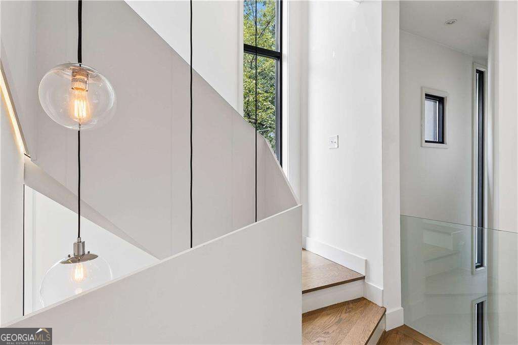 Modern stairwell with wood steps, glass railing, tall windows, and globe pendant lights.
