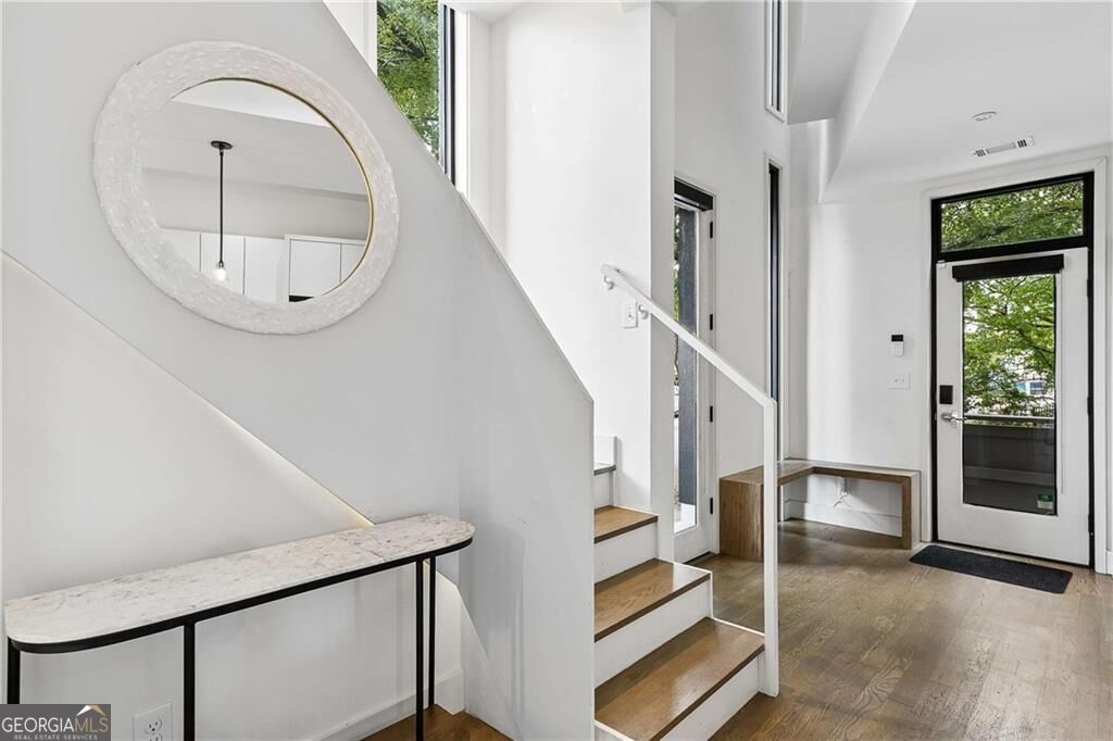 Bright entryway with a wood staircase, round mirror, and glass front door.
