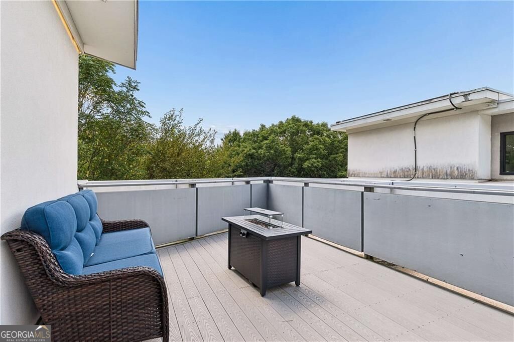 Rooftop deck with blue-cushioned wicker seating and a fire table overlooking trees.